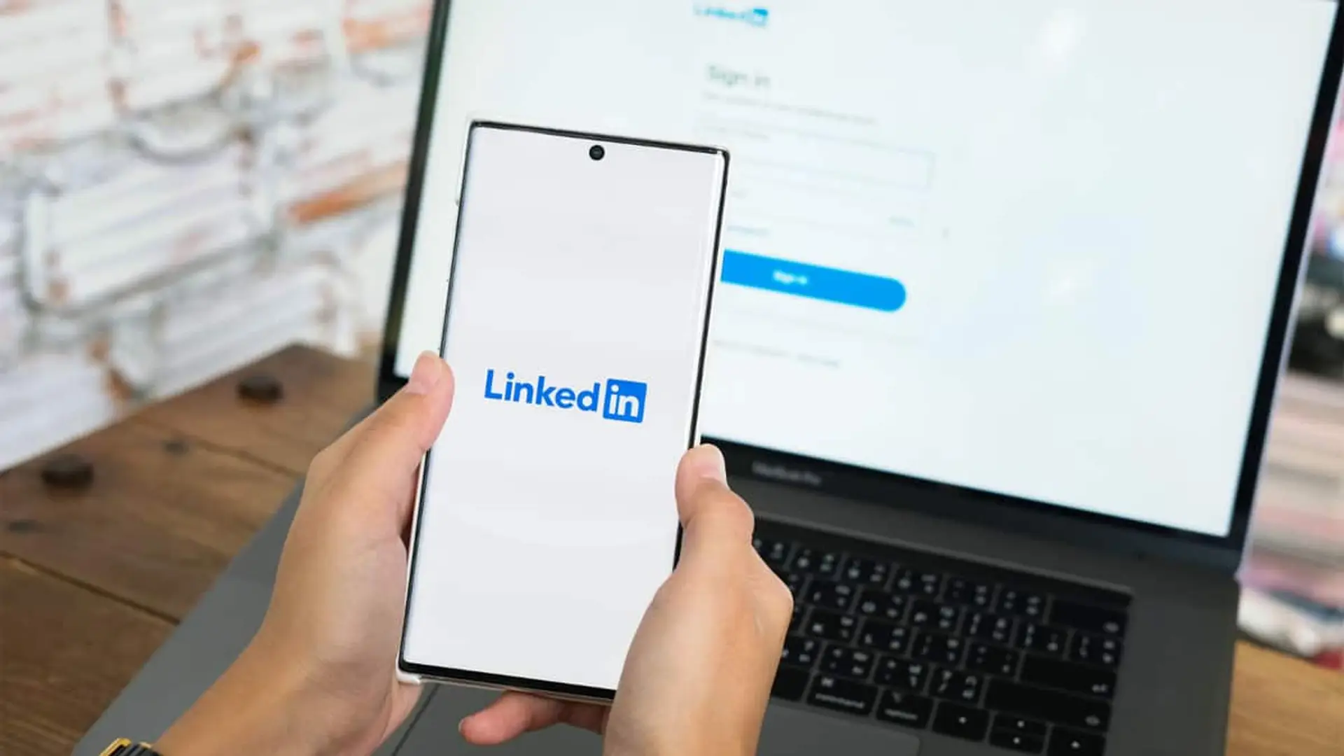 Así te roban en LinkedIn: el mensaje del reclutador perfecto que en realidad es una mafia Inicio de sesión en LinkedIn desde el móvil con un ordenador portátil al fondo