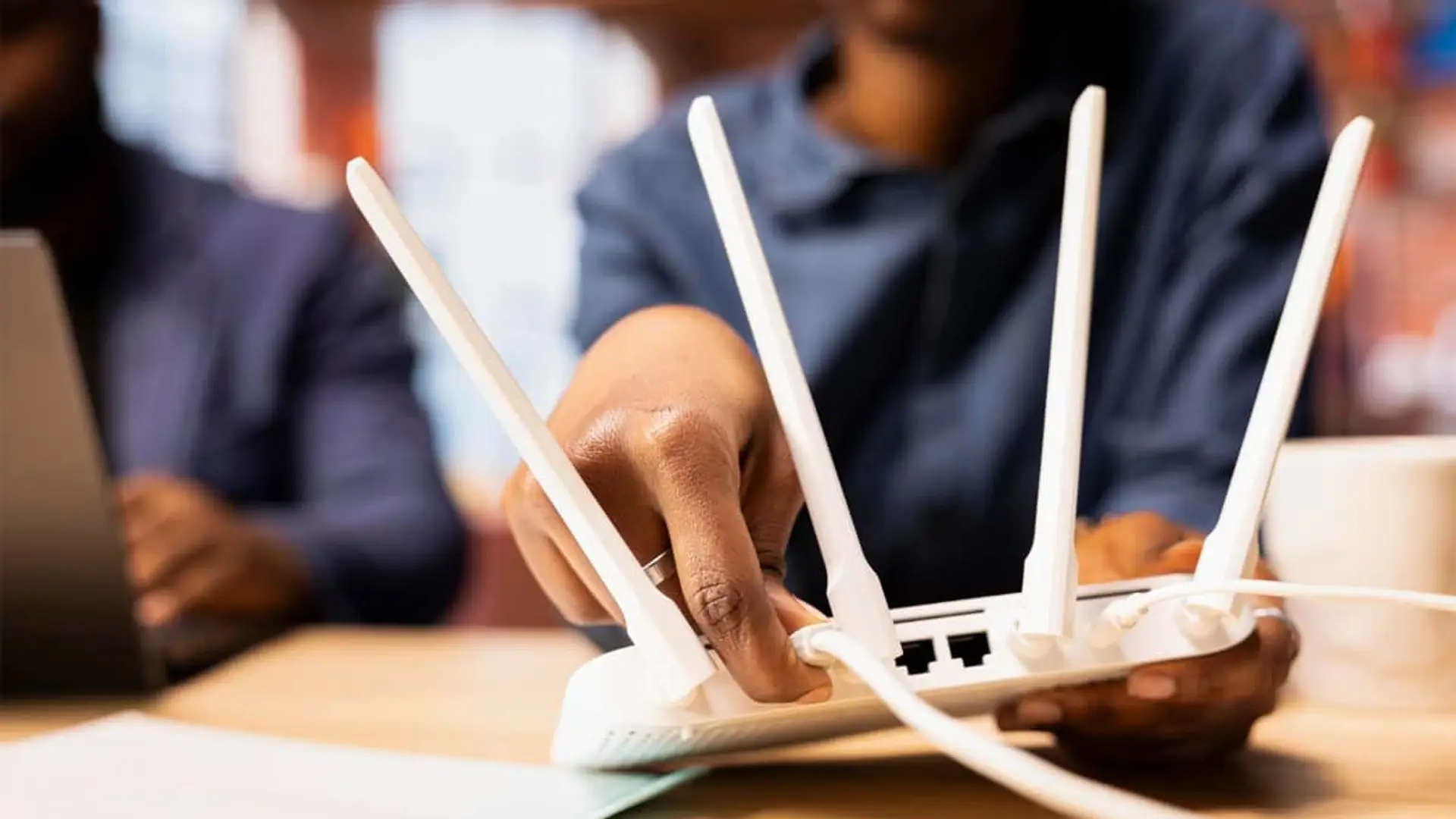 Persona conectando cables a un router Wi-Fi susceptible de ser hackeado por ciberdelincuentes.