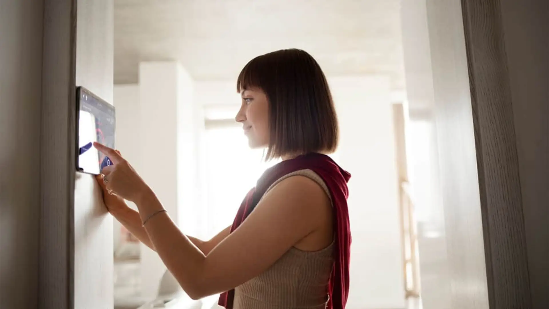 Mujer joven utilizando un panel de alarma en la pared para controlar la seguridad de su hogar inteligente.