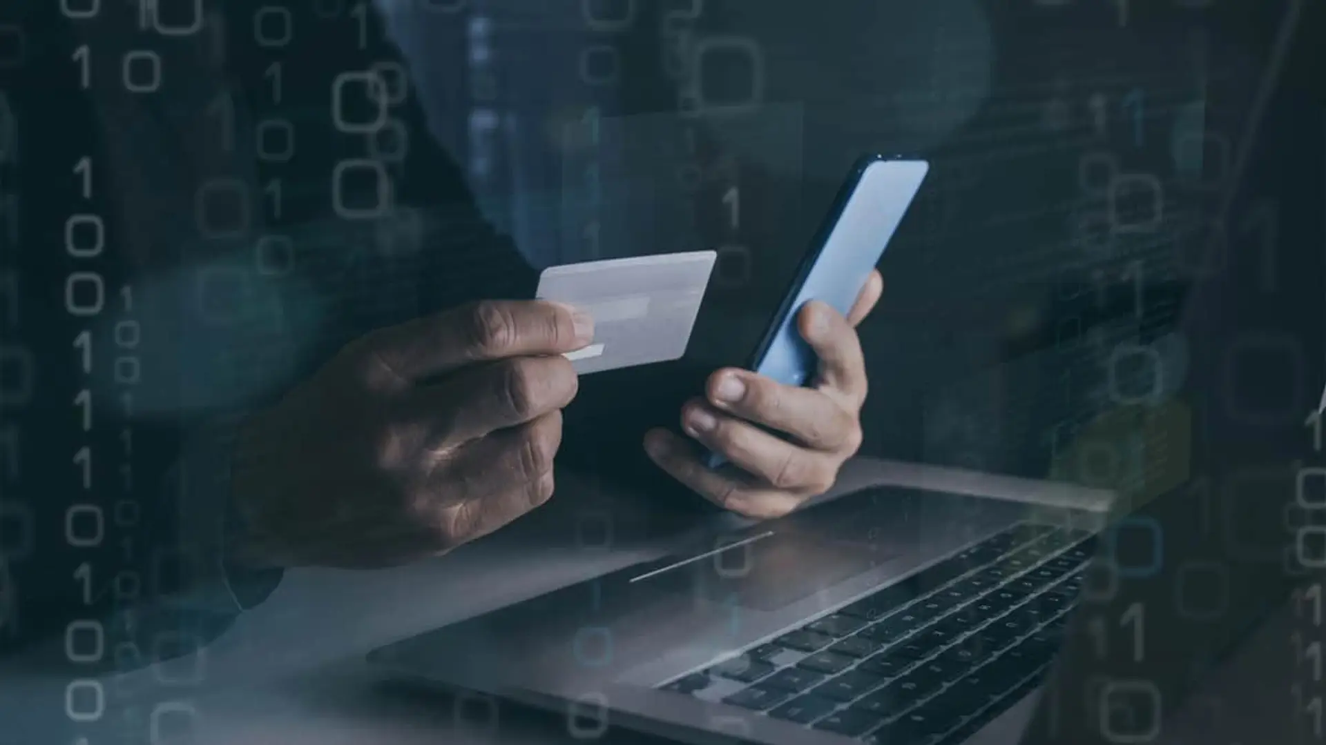 Ciberseguridad y fraude online: manos con tarjeta de crédito y móvil rodeadas de código binario y datos digitales.