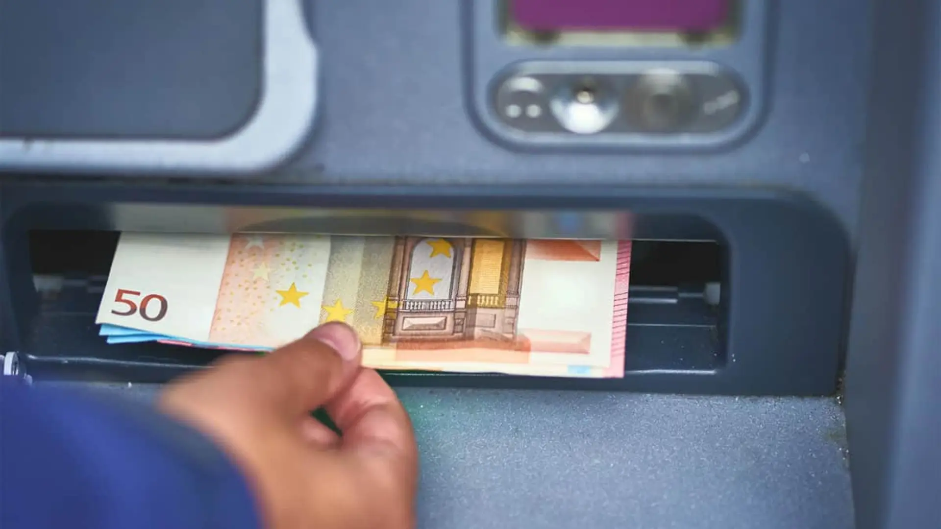 Mano retirando billetes de cincuenta euros del dispensador de un cajero automático como concepto de dinero en efectivo.