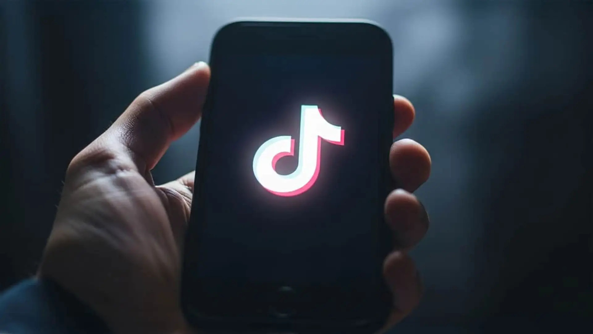 Experto en seguridad advierte: ojo con estos vídeos de TikTok, son una trampa para robar tus datos Mano sosteniendo un móvil con el logo de la red social TikTok iluminado en la pantalla.