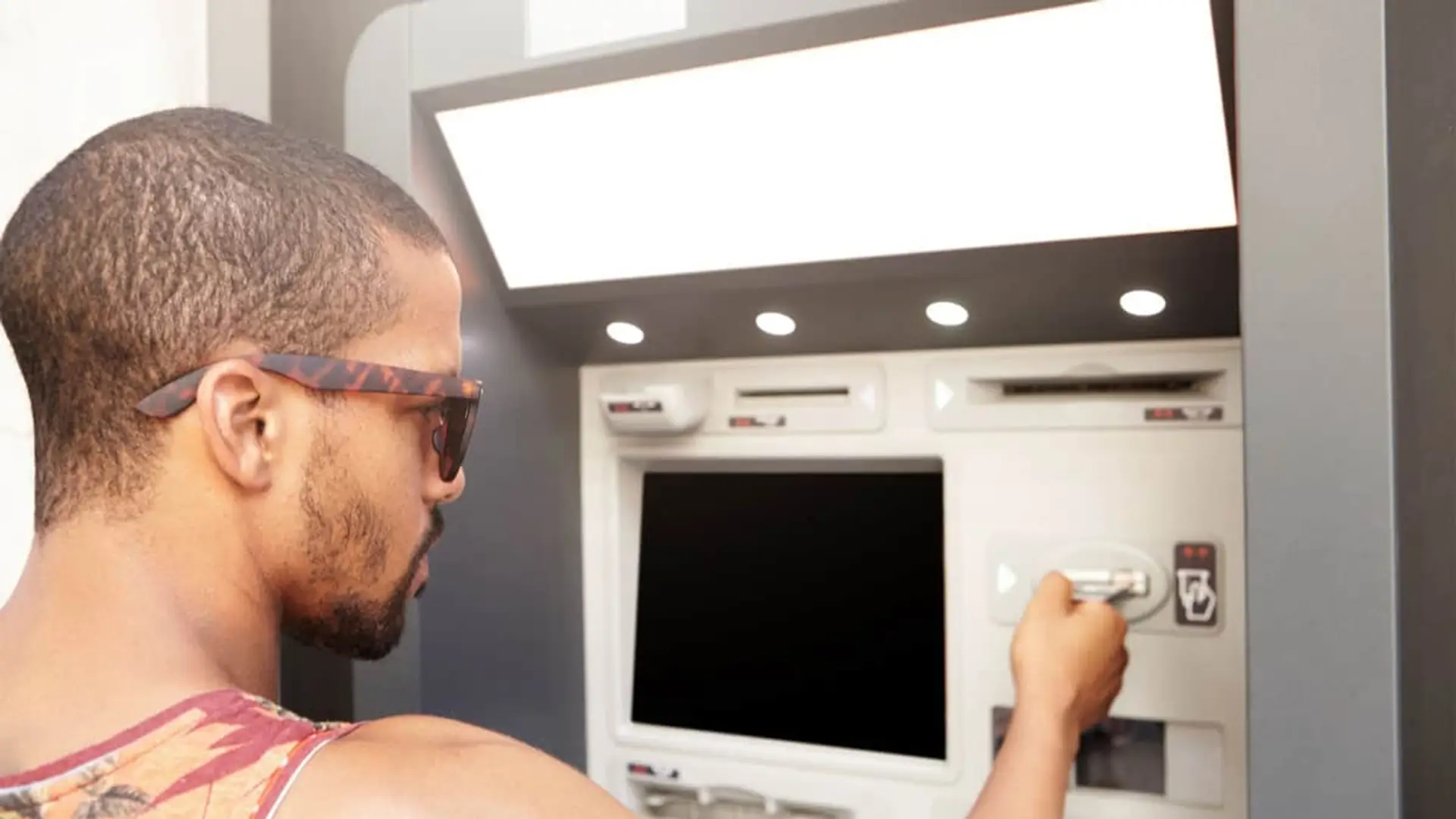 Hombre con gafas de sol introduciendo su tarjeta bancaria en un cajero automático para realizar gestiones financieras.