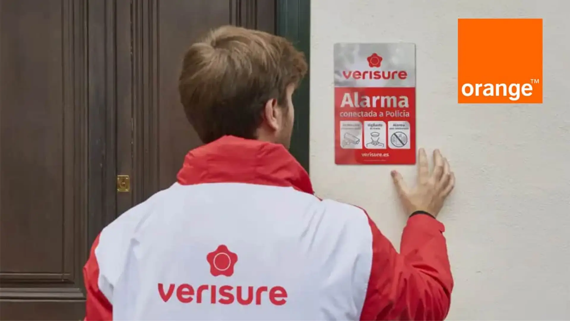 Técnico instalando una placa de alarma de Verisure y Orange conectada a Policía en la entrada de una casa.
