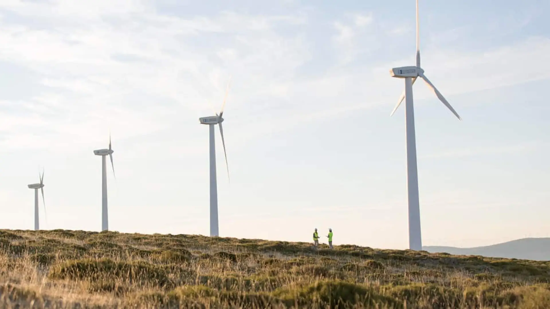 Varios aerogeneradores en un paisaje abierto con dos técnicos caminando en primer plano