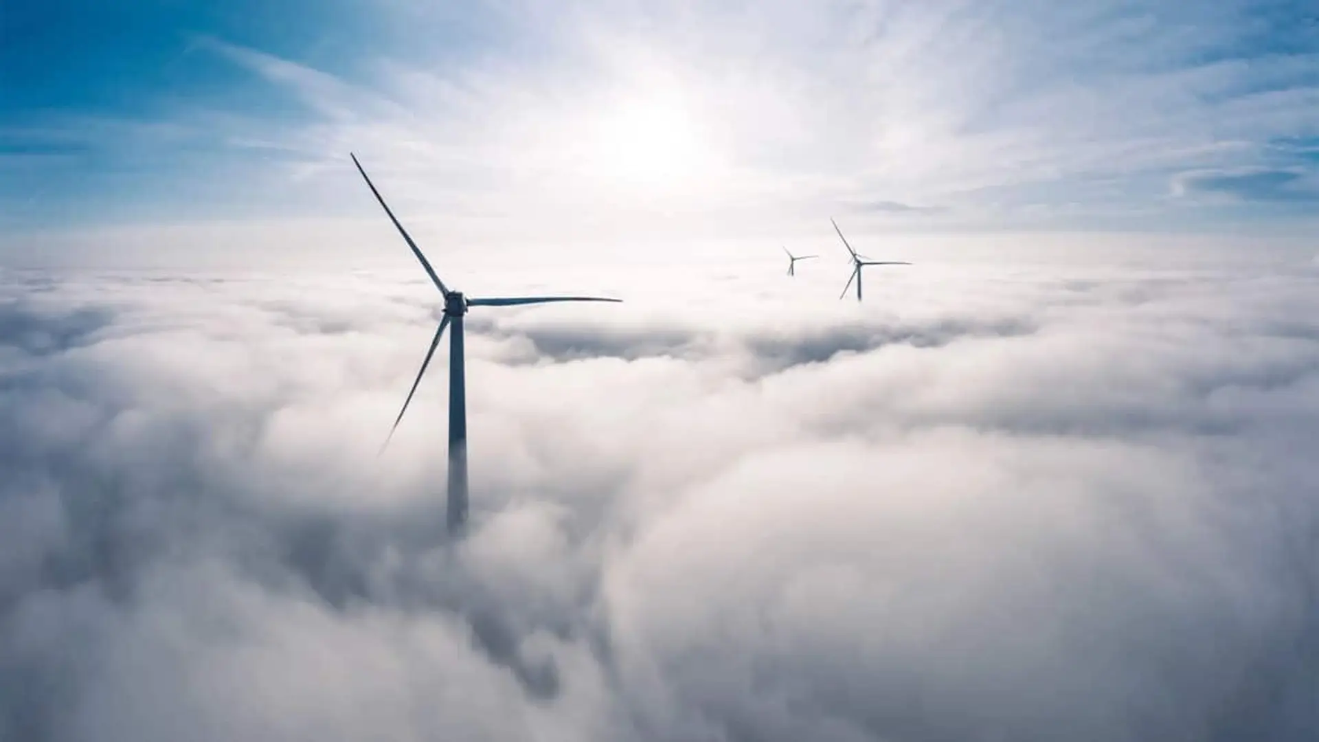 Aerogeneradores sobresaliendo entre nubes en un parque eólico.