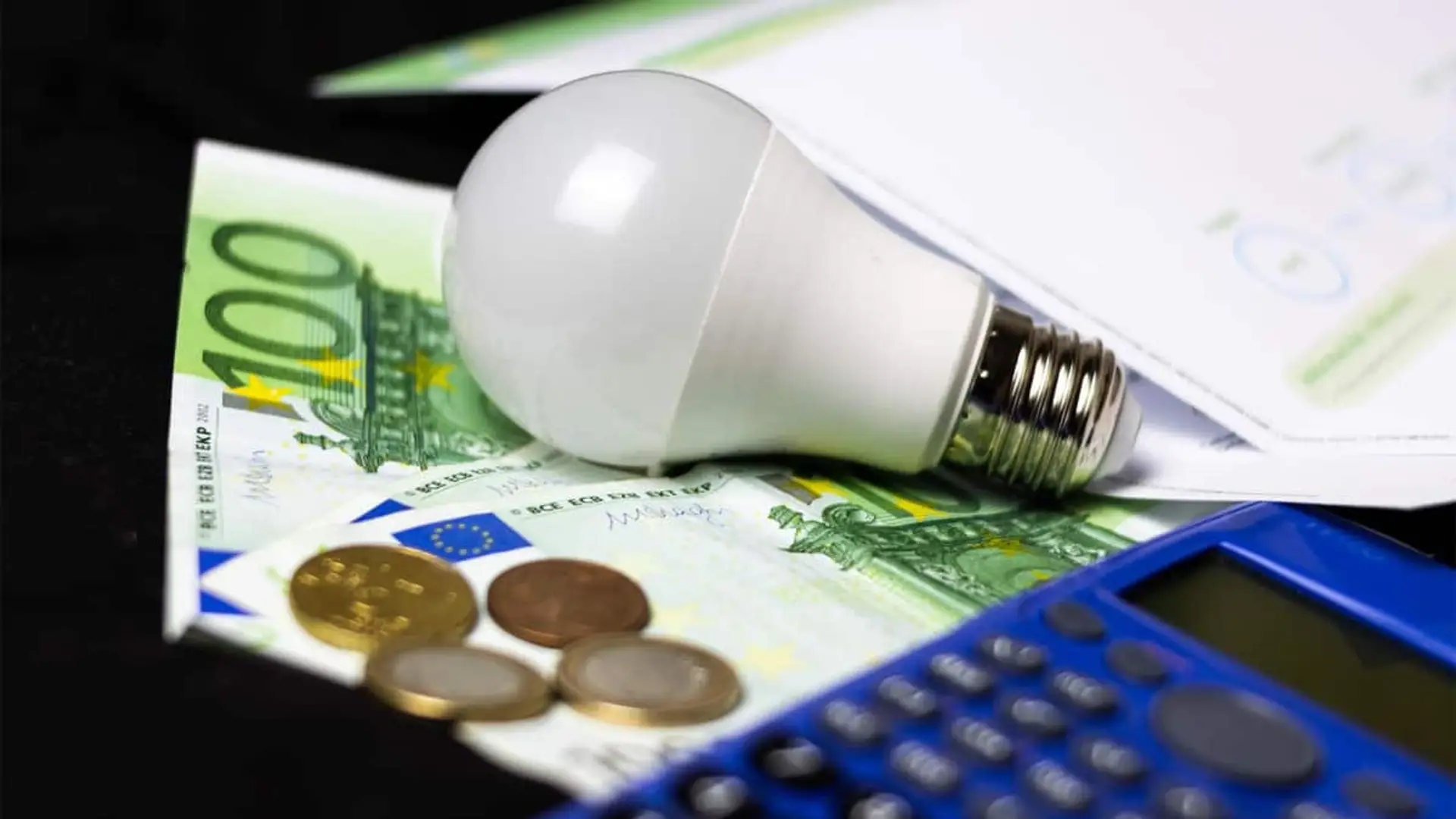 Bombilla sobre billetes y monedas de euro junto a una calculadora, símbolo del ahorro en la factura de la luz