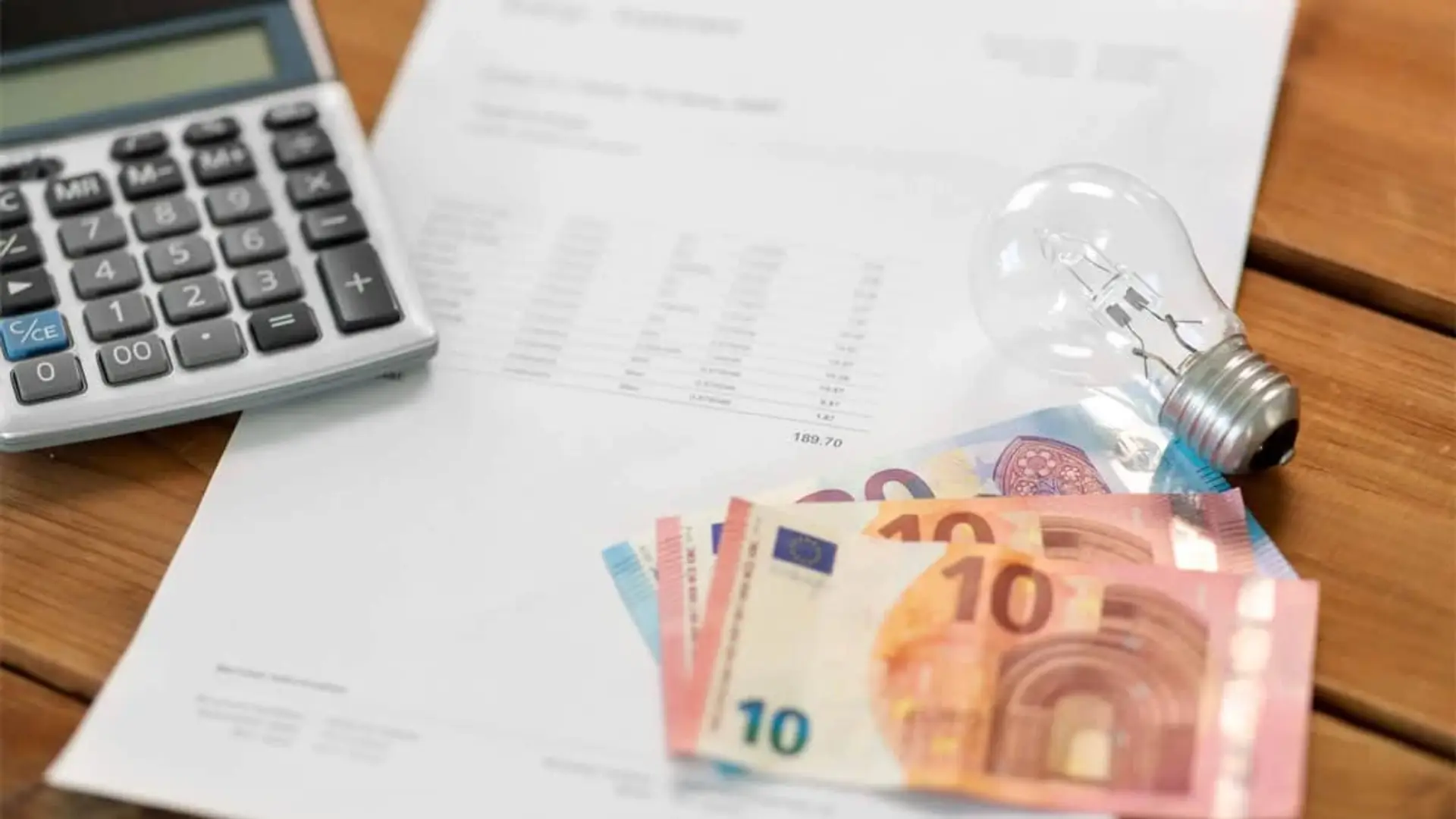 Los españoles pagan 2 millones de euros extra al día para evitar un nuevo apagón Billetes de euro, una bombilla y una calculadora sobre una factura de electricidad.