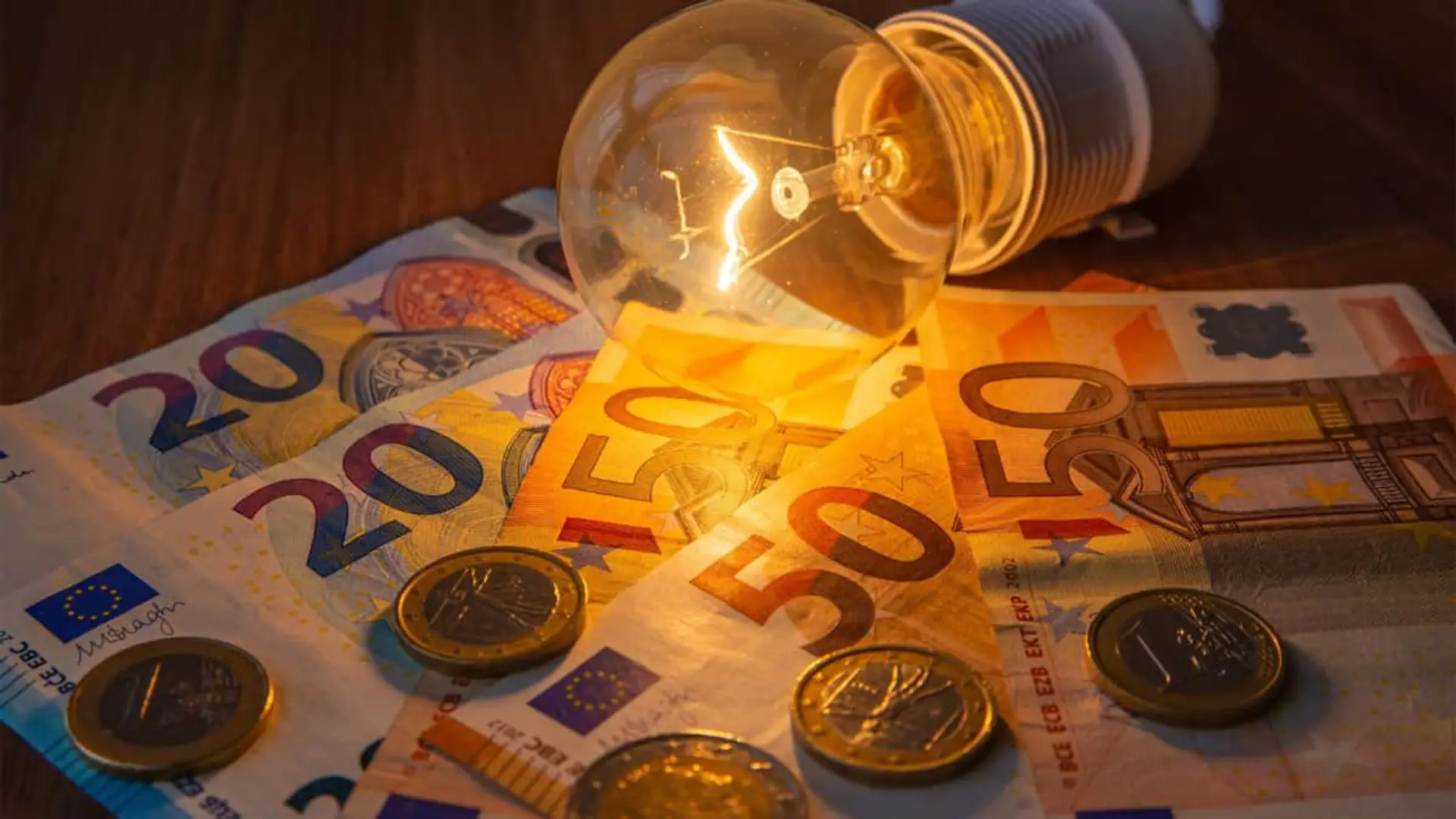 Bombilla encendida colocada sobre billetes y monedas de euro