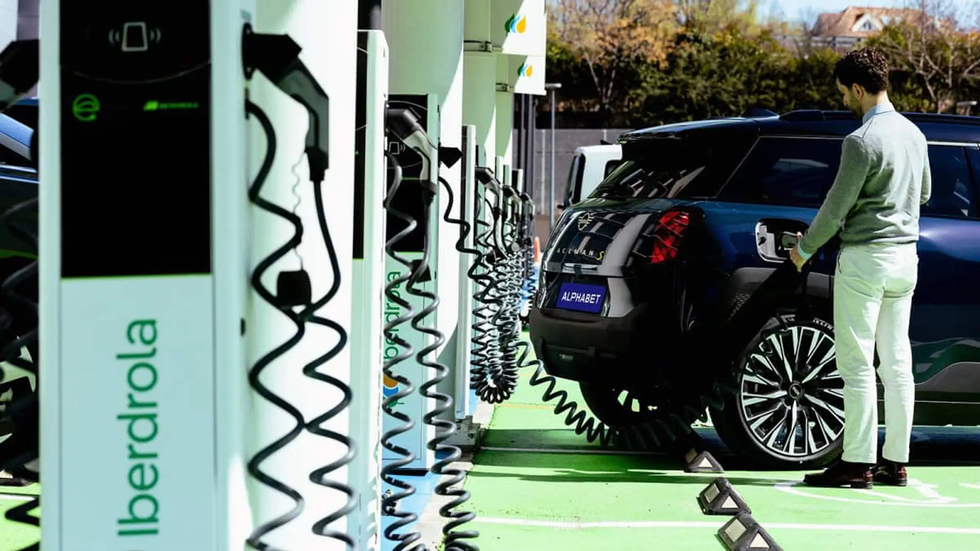 Varios cargadores eléctricos de Iberdrola en serie con un hombre conectando su coche en una estación de recarga.