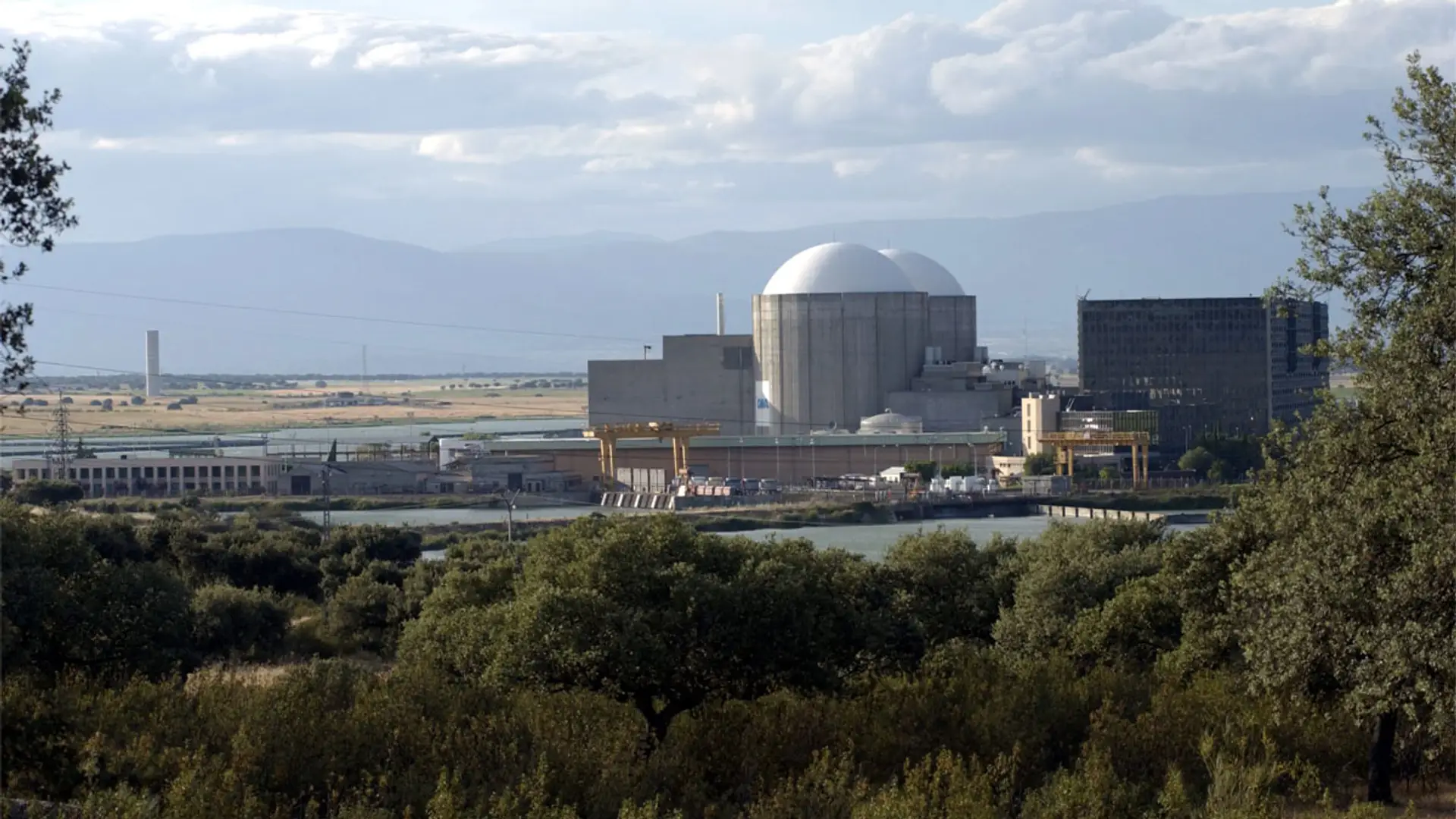 Vista de la central nuclear de Almaraz desde un entorno rural con árboles en primer plano