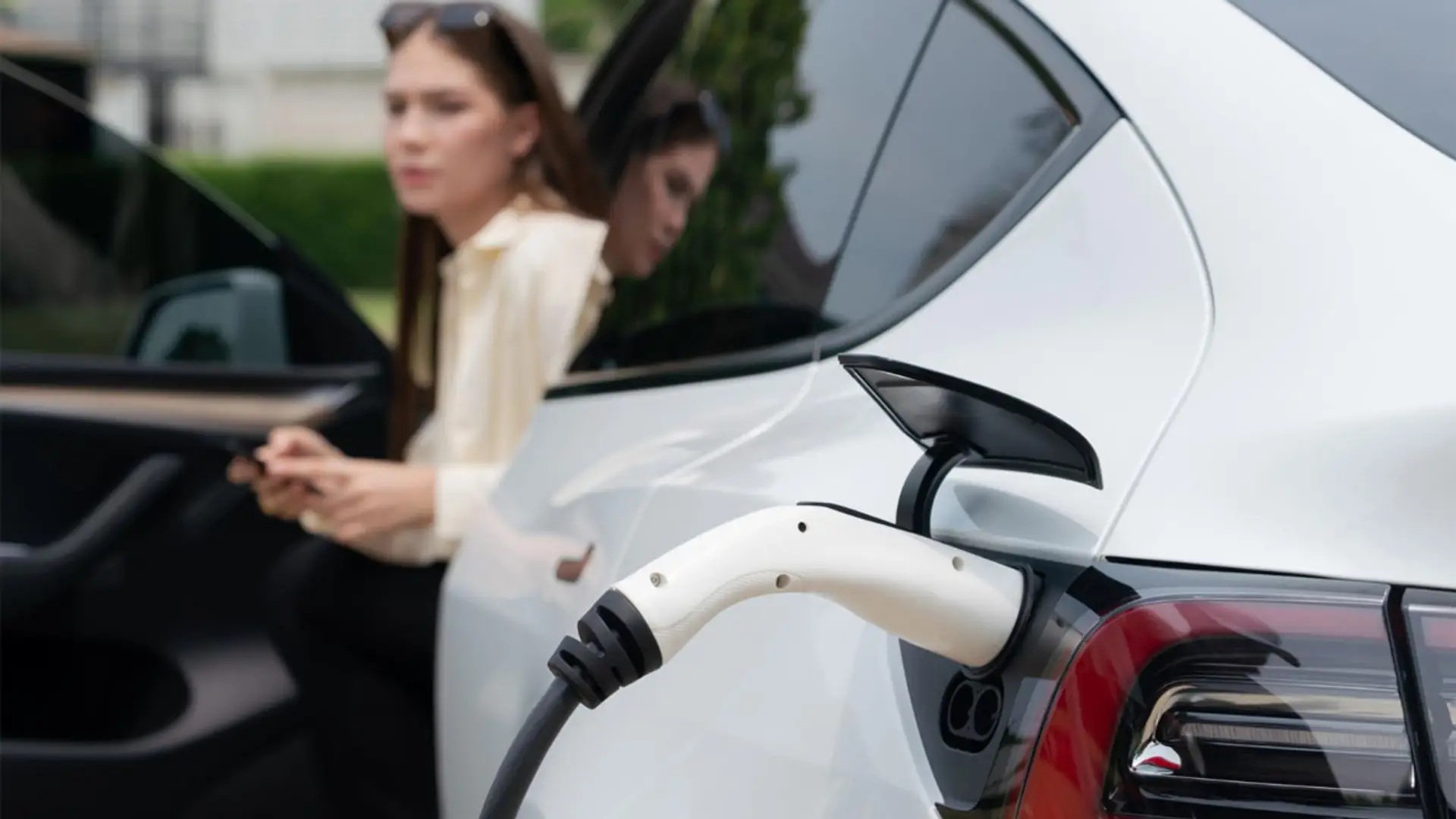 Coche eléctrico blanco conectado a un cargador con una mujer al fondo