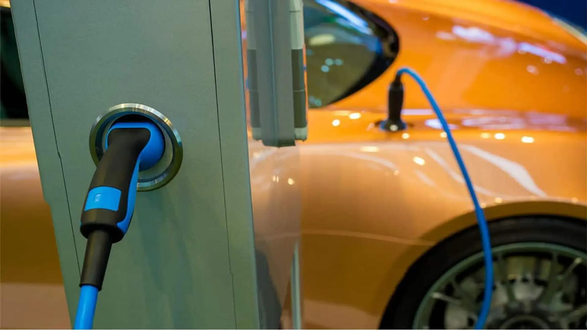 España se corona líder del coche eléctrico en Europa: las ventas se disparan hasta un 105% Detalle de un coche eléctrico cargando en una estación pública con cable azul.