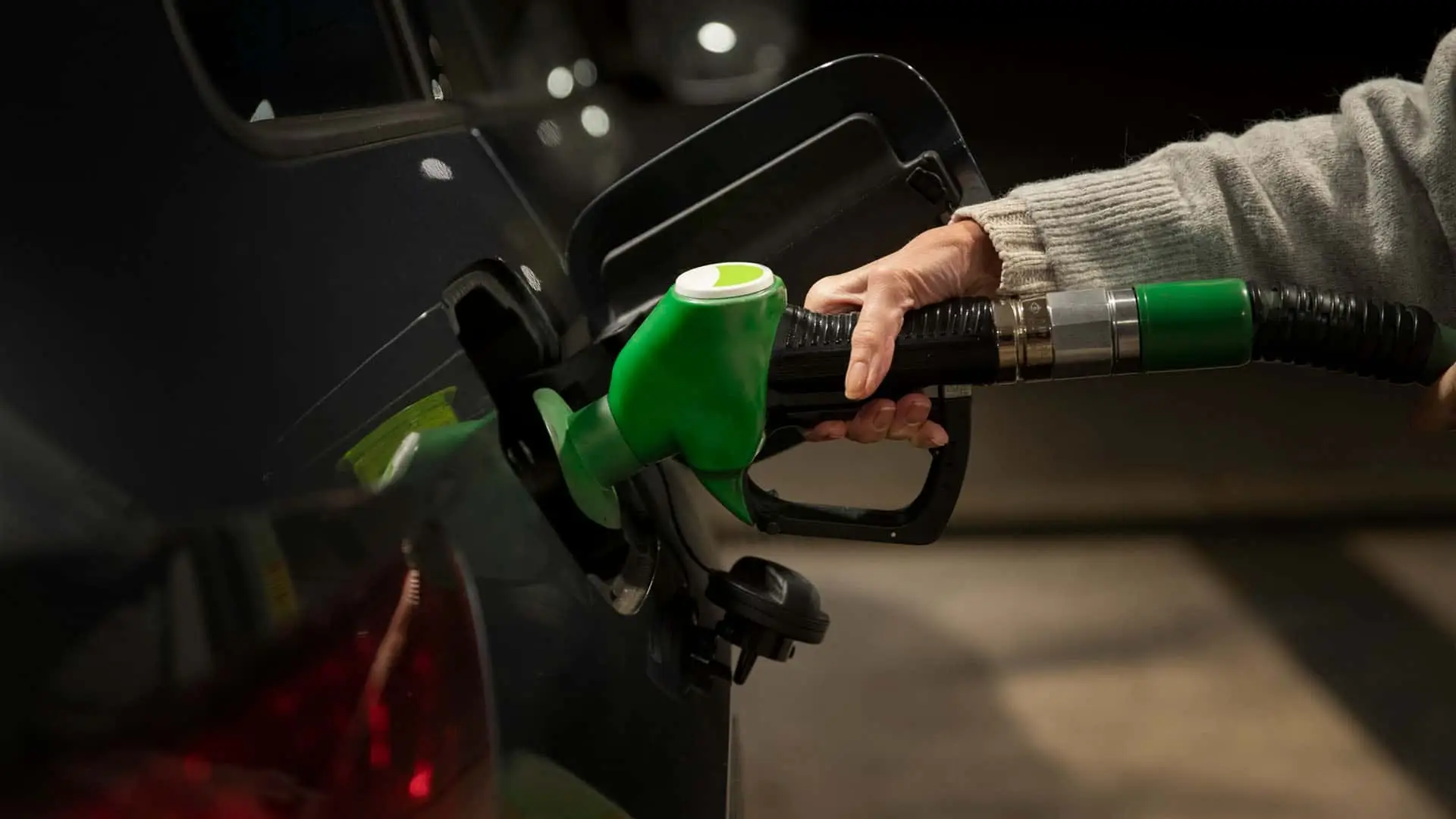 Persona repostando gasolina en un coche con una manguera de color verde en una gasolinera.