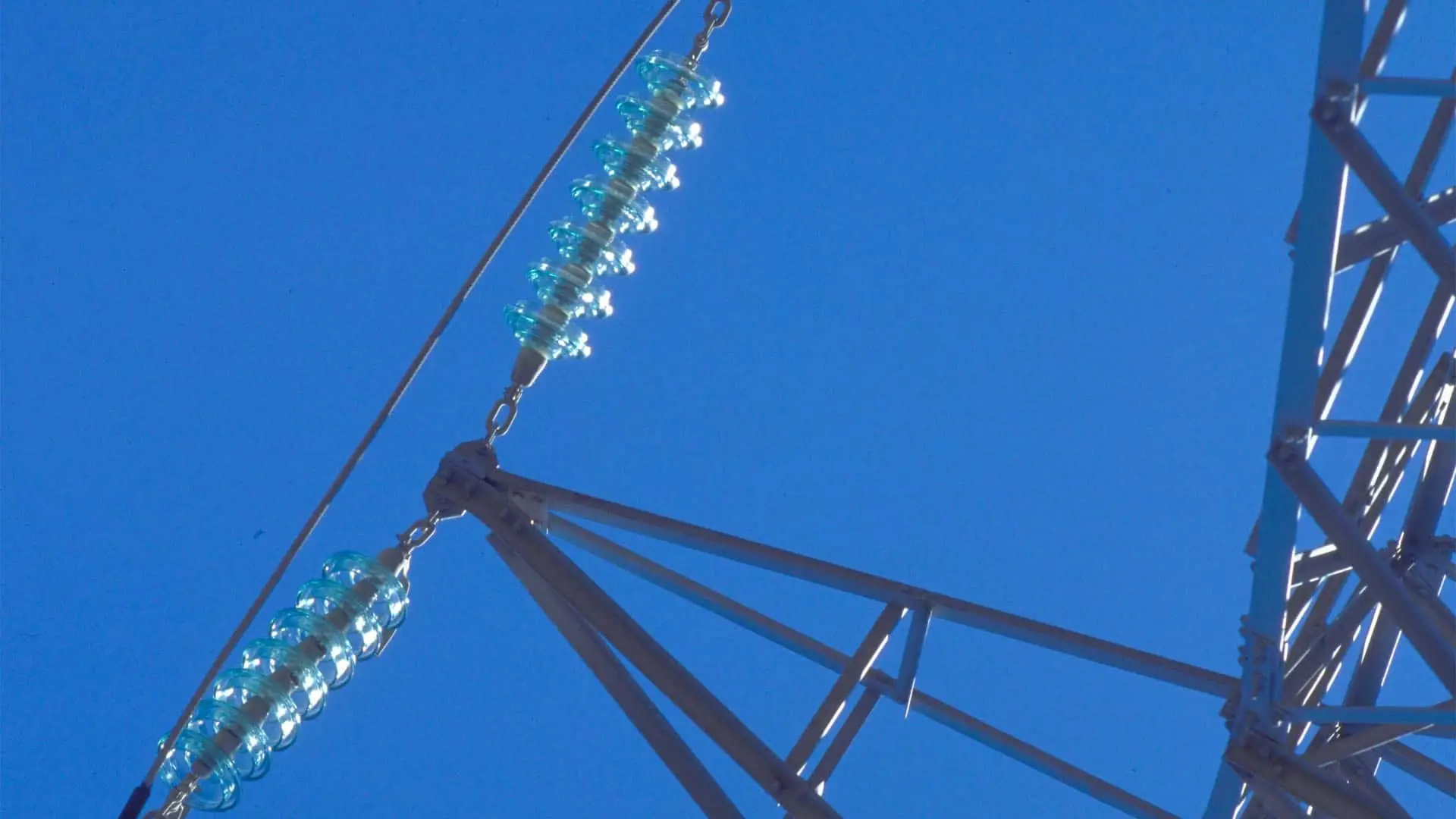 Detalle de aisladores en torre eléctrica sobre cielo azul despejado.