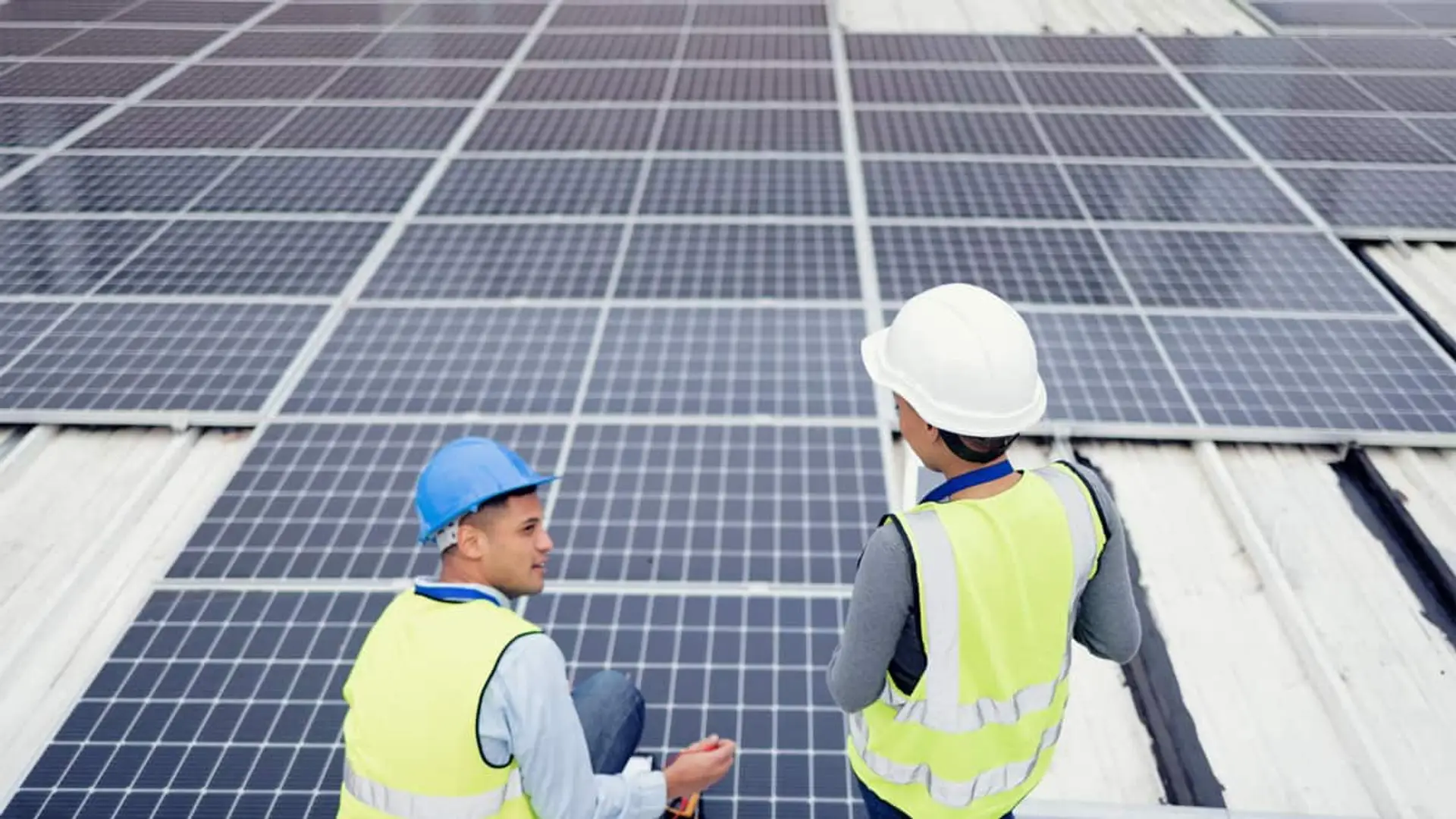 Dos técnicos con casco y chaleco reflectante junto a paneles solares en una cubierta