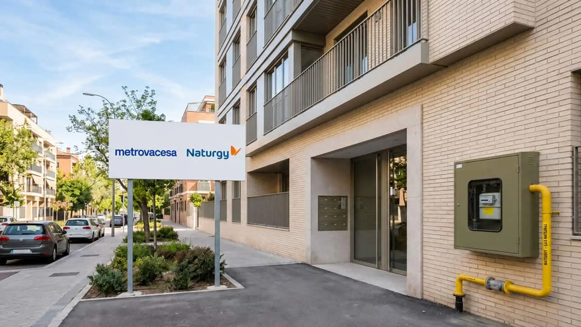Naturgy y Metrovacesa preparan para el gas verde más de 430 viviendas nuevas en Madrid y A Coruña Edificio residencial con cartel de Metrovacesa y Naturgy junto a una instalación de gas en la fachada