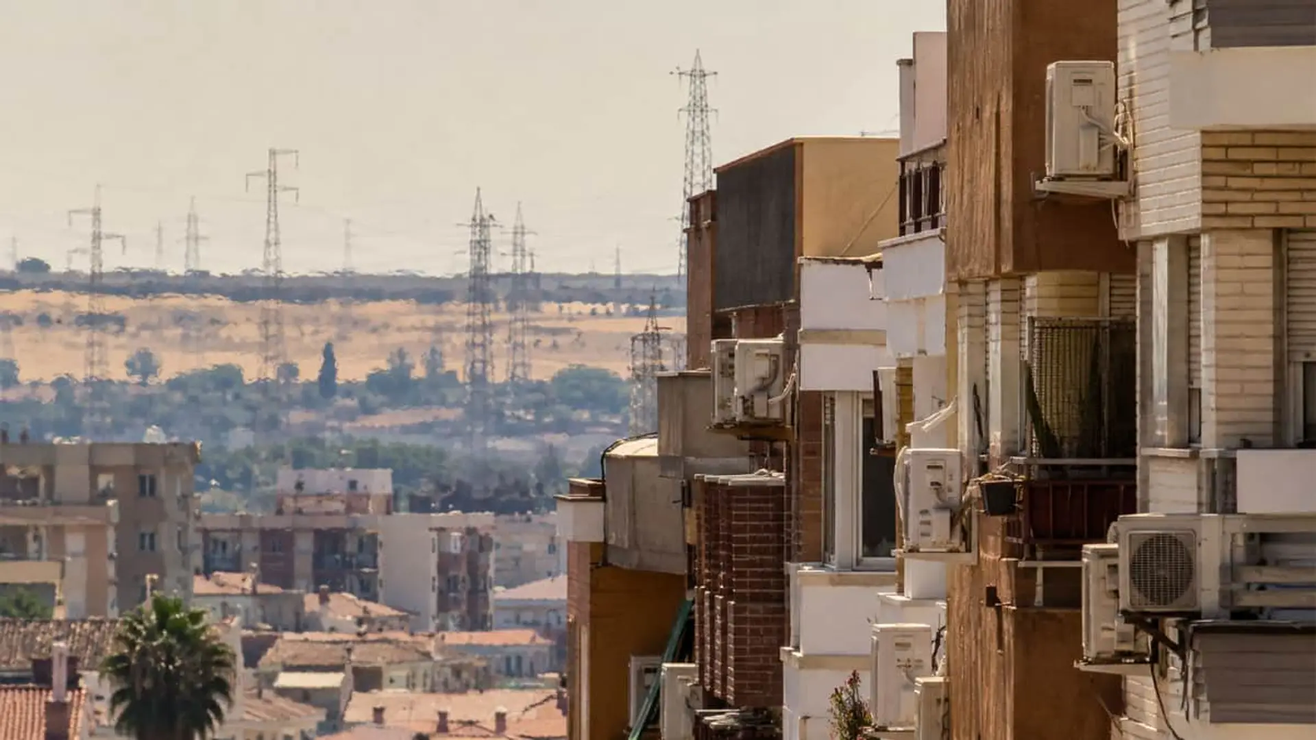 Edificios residenciales con aire acondicionado y torres eléctricas de alta tensión al fondo.