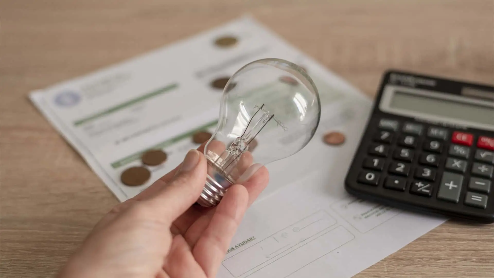 Persona sosteniendo una bombilla junto a una factura de luz y una calculadora.