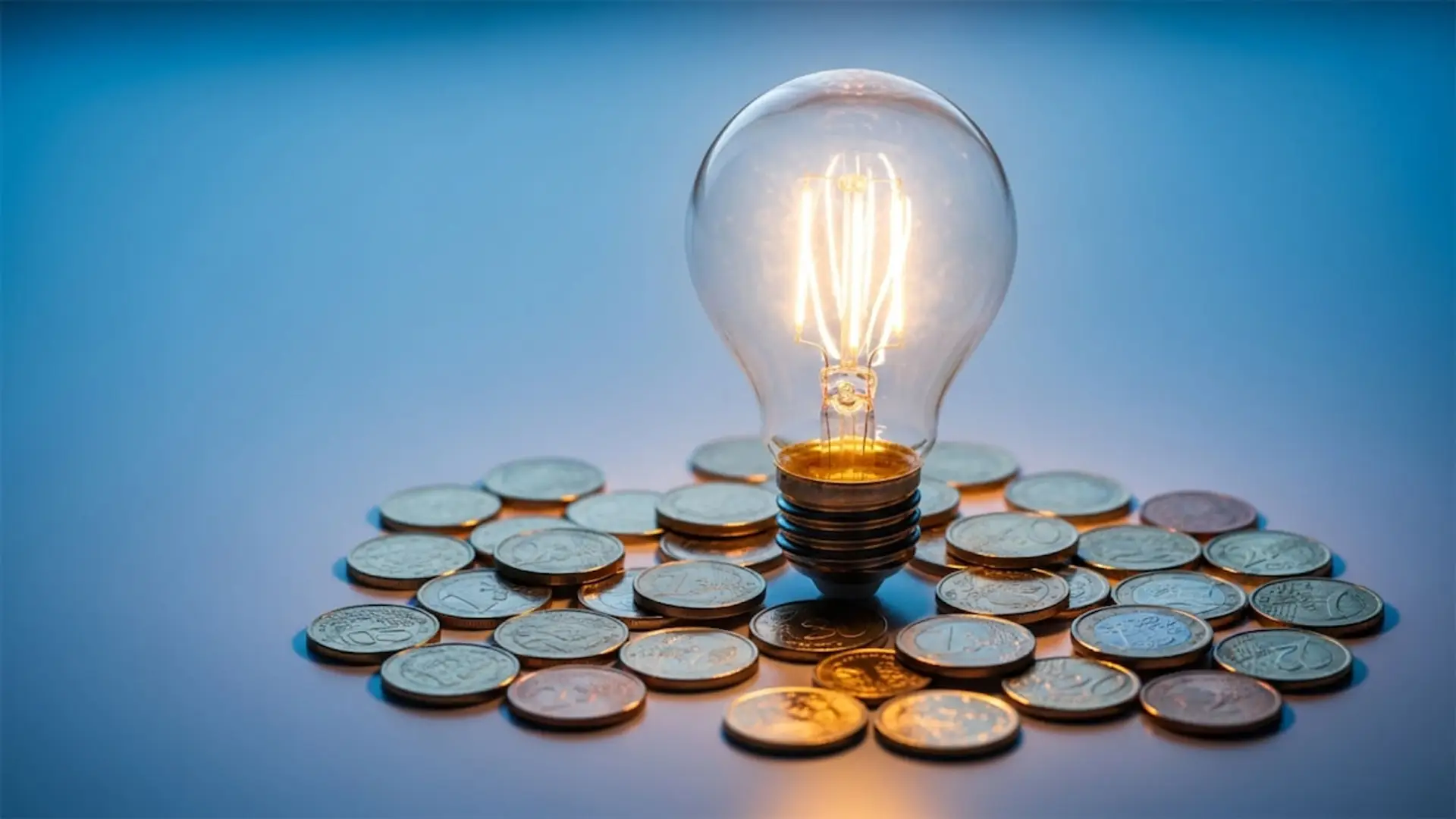 FACUA alerta: este es el truco de las eléctricas para inflar tu factura de la luz Bombilla encendida sobre un montón de monedas, simbolizando el coste de la energía y el precio de la factura de la luz.
