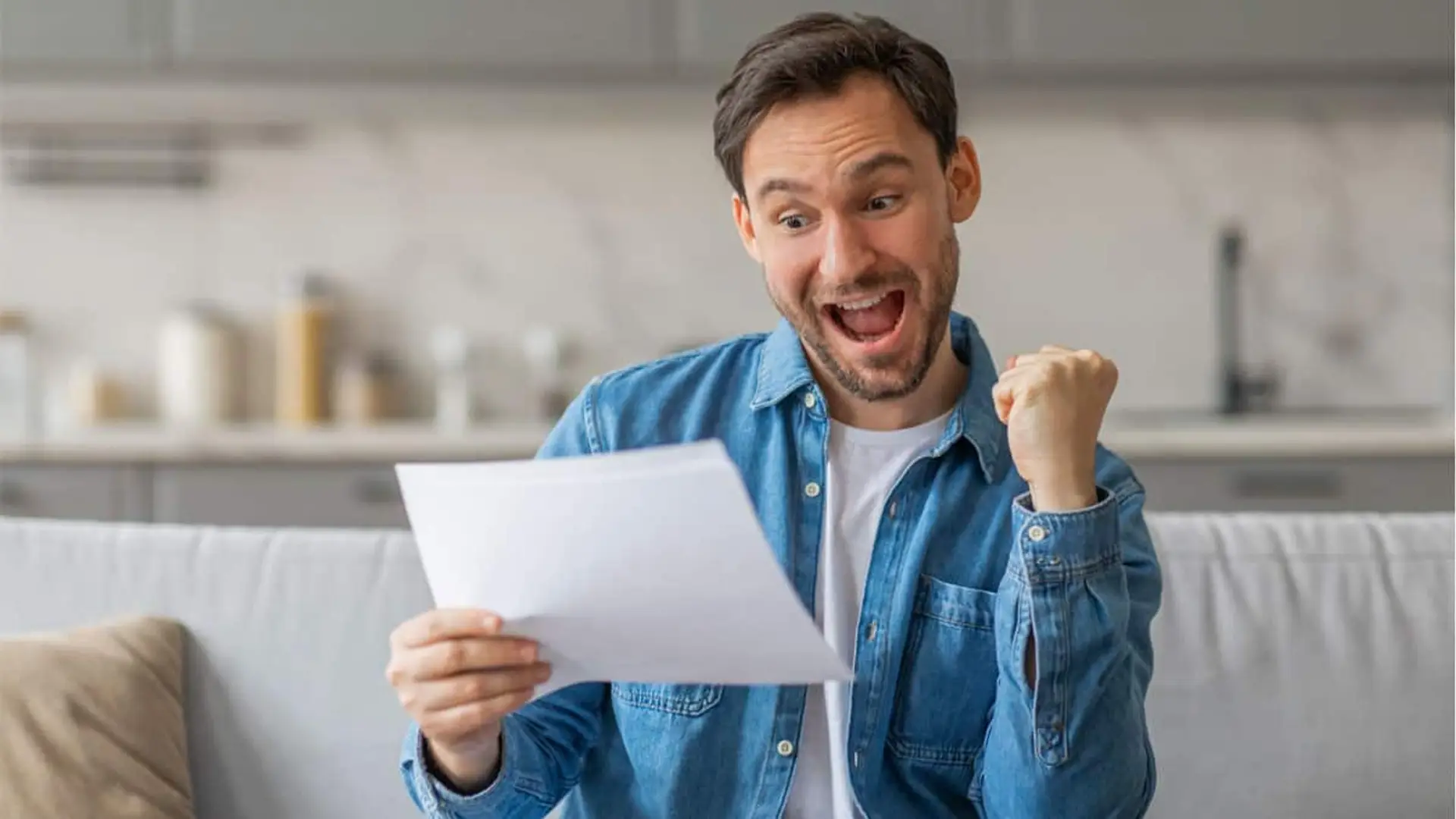 Hombre alegre leyendo un documento en casa con el puño levantado