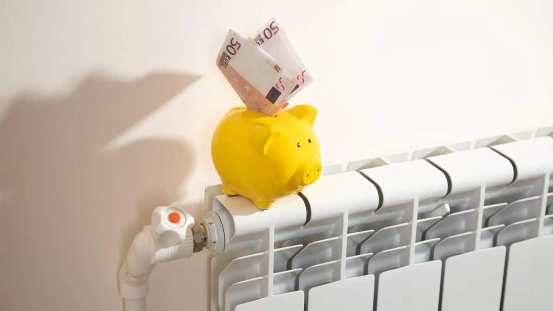 Hucha amarilla sobre un radiador con varios billetes de euro