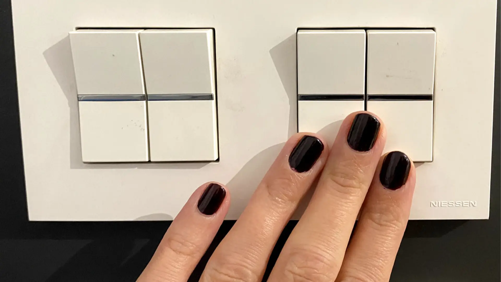 Una mano femenina con las uñas pintadas apaga un interruptor de luz.