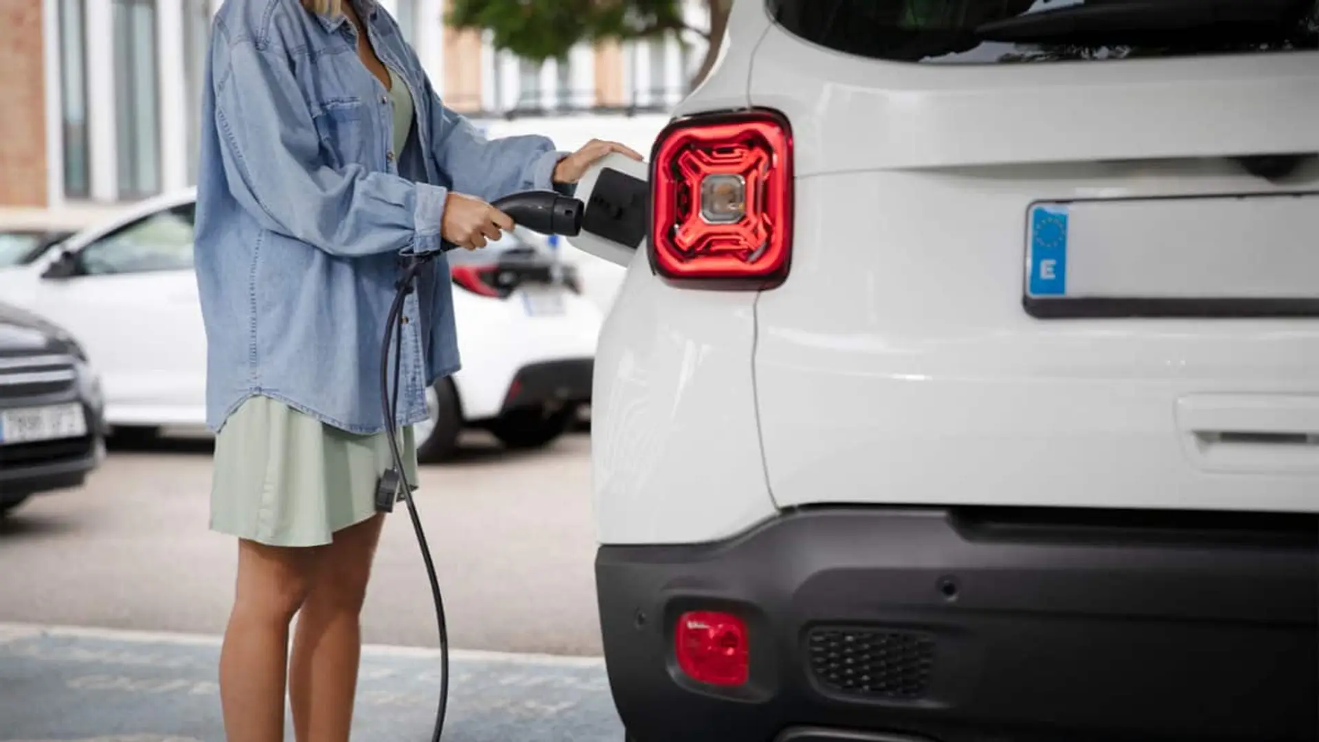 Octopus y Ford se alían para impulsar el coche eléctrico con recargas gratuitas y bonificaciones especiales Mujer cargando un coche eléctrico blanco en un punto de carga urbano.