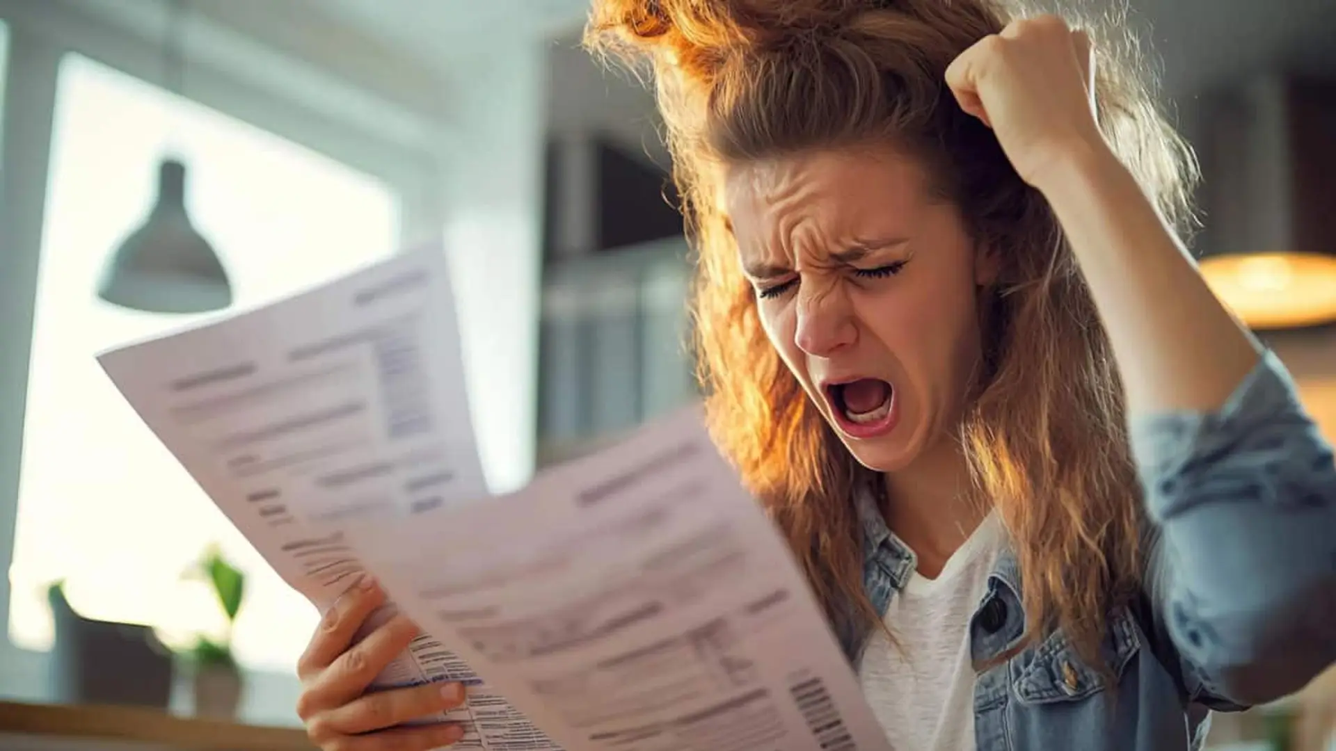 Mujer enfadada revisando varias facturas mientras levanta el puño