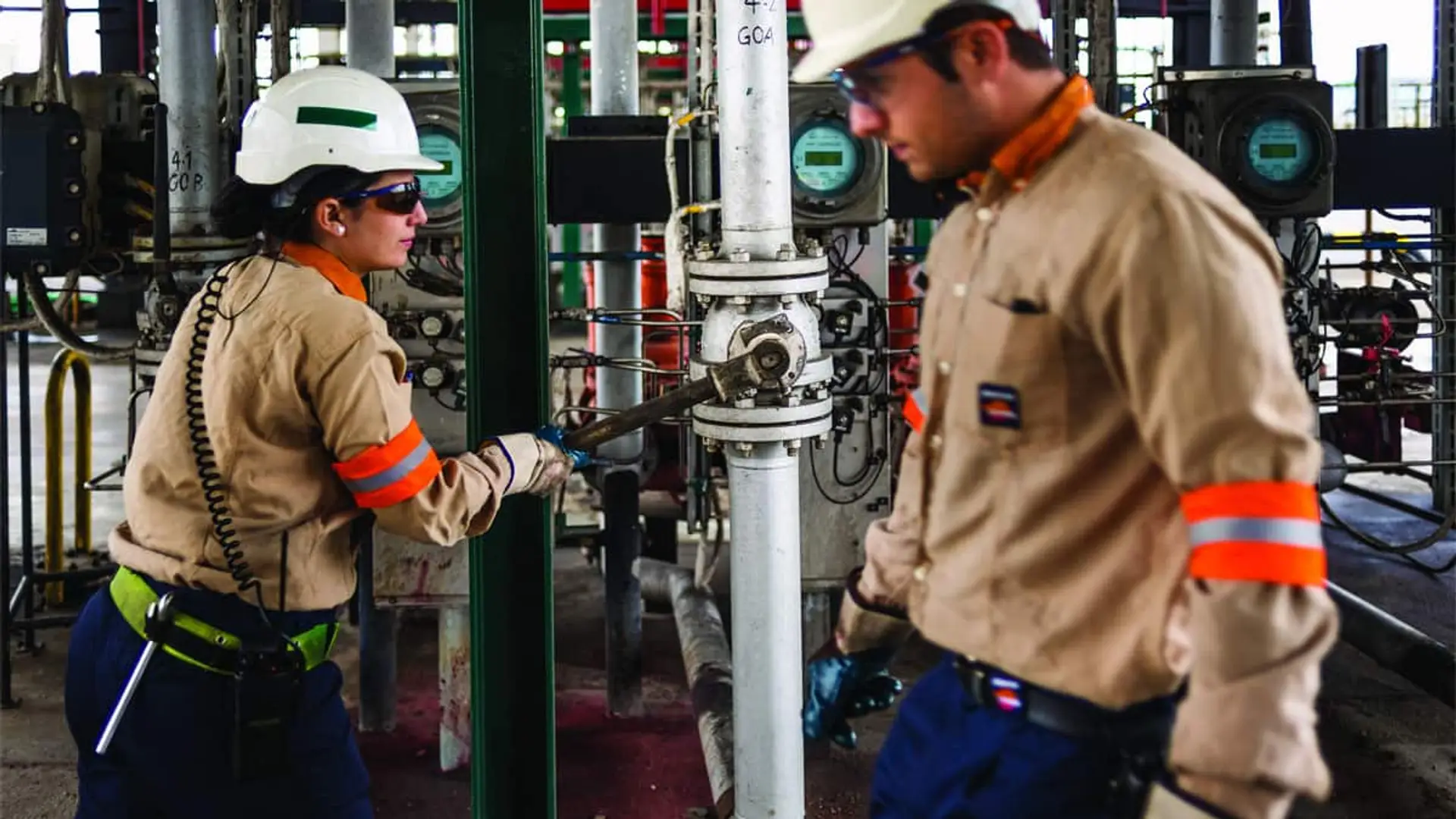 Dos operarios de Repsol con casco trabajando junto a tuberías e instrumentación en unas instalaciones industriales