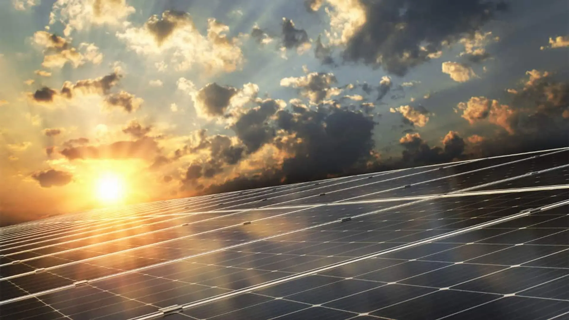 Filas de paneles solares con el sol bajo entre nubes