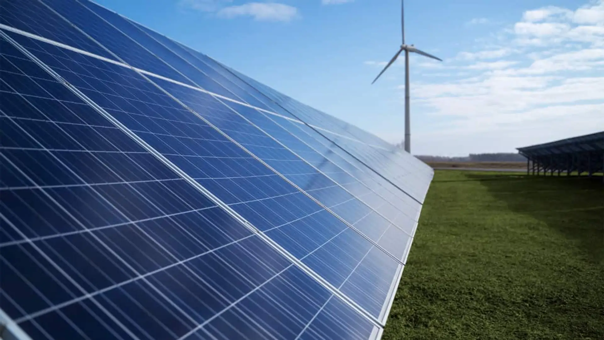 Paneles solares instalados en un campo con un aerogenerador al fondo en un día despejado.