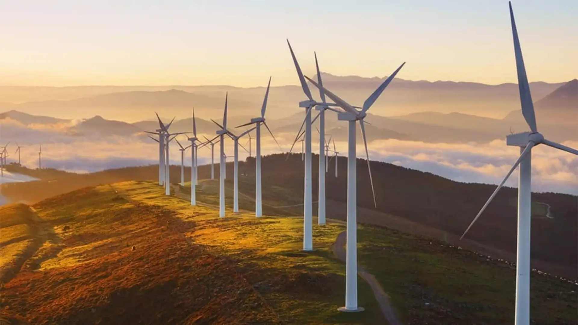 Fila de aerogeneradores en un parque eólico de montaña iluminado por el amanecer entre nubes.