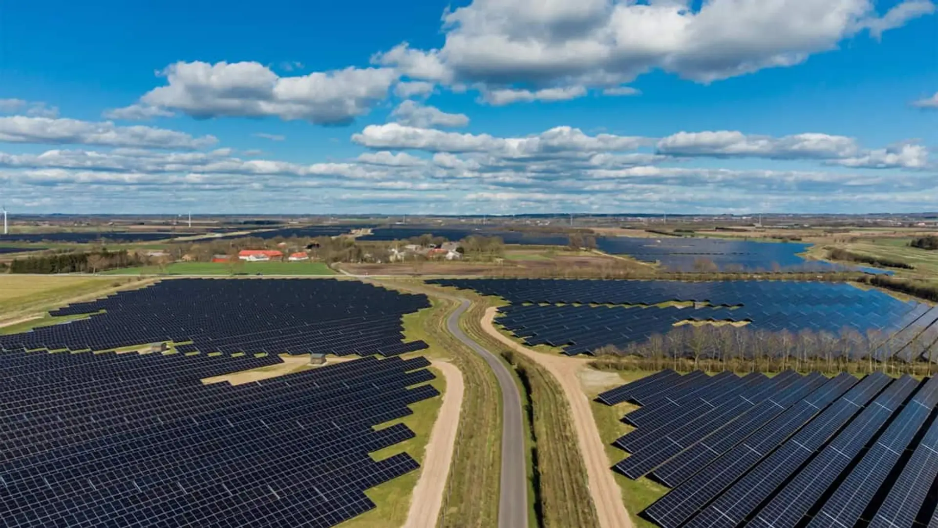 Vista aérea de un parque solar con paneles fotovoltaicos junto a aerogeneradores en un entorno rural.