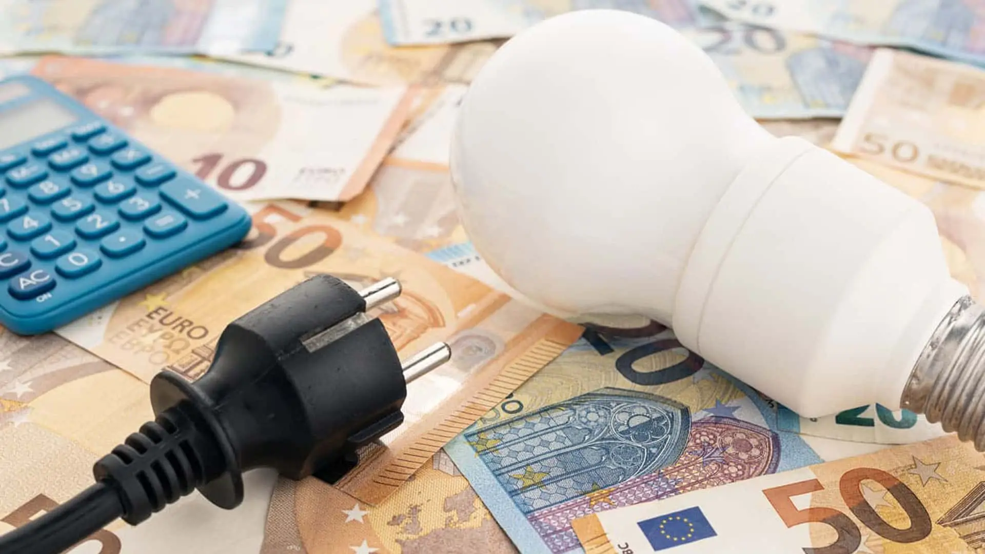 Bombilla, enchufe y calculadora sobre billetes de euro representando el coste de la electricidad.