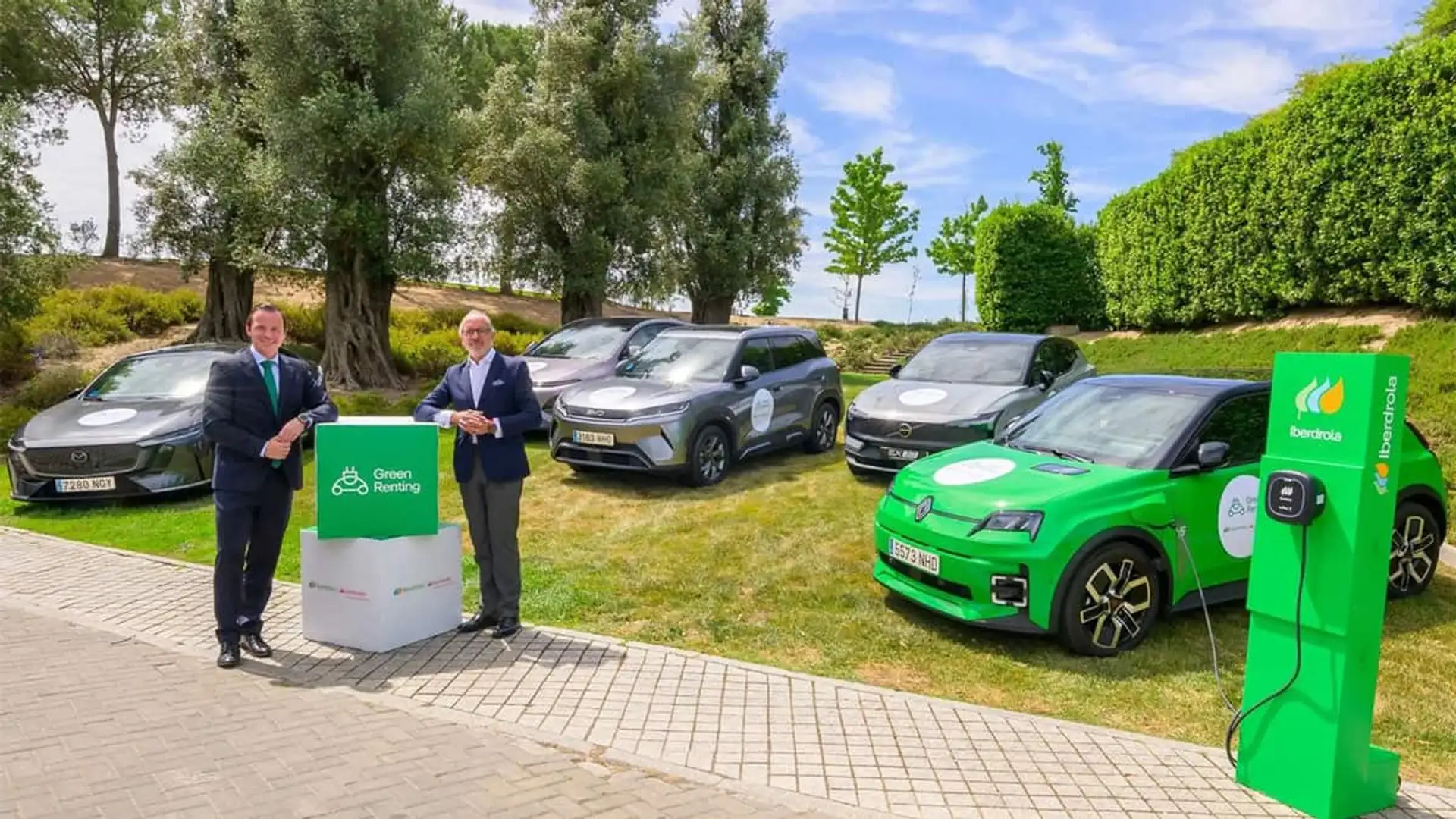 Dos hombres junto a varios coches eléctricos y un punto de recarga de Iberdrola en una presentación de Green Renting