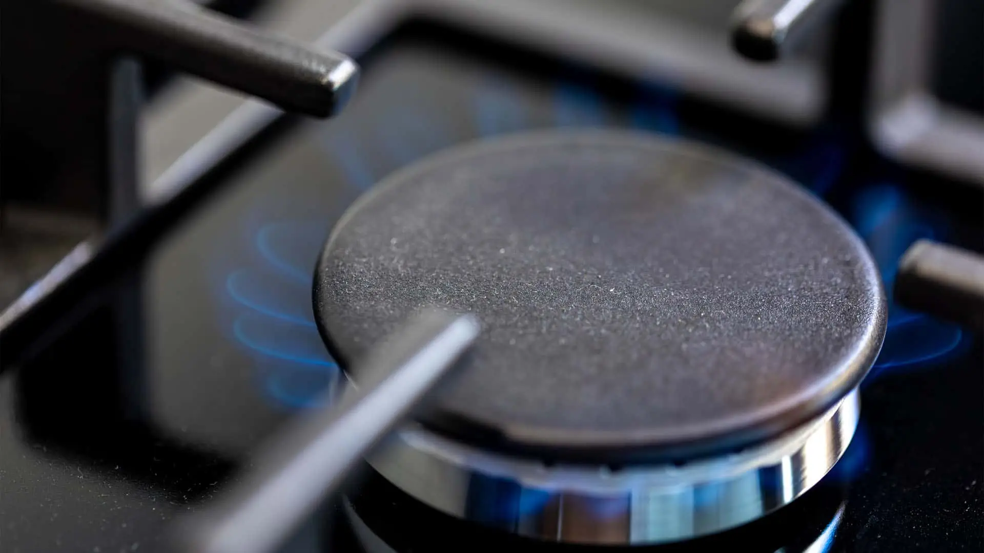 Primer plano de un quemador de una cocina de gas con la llama azul encendida, mostrando el consumo de gas natural.
