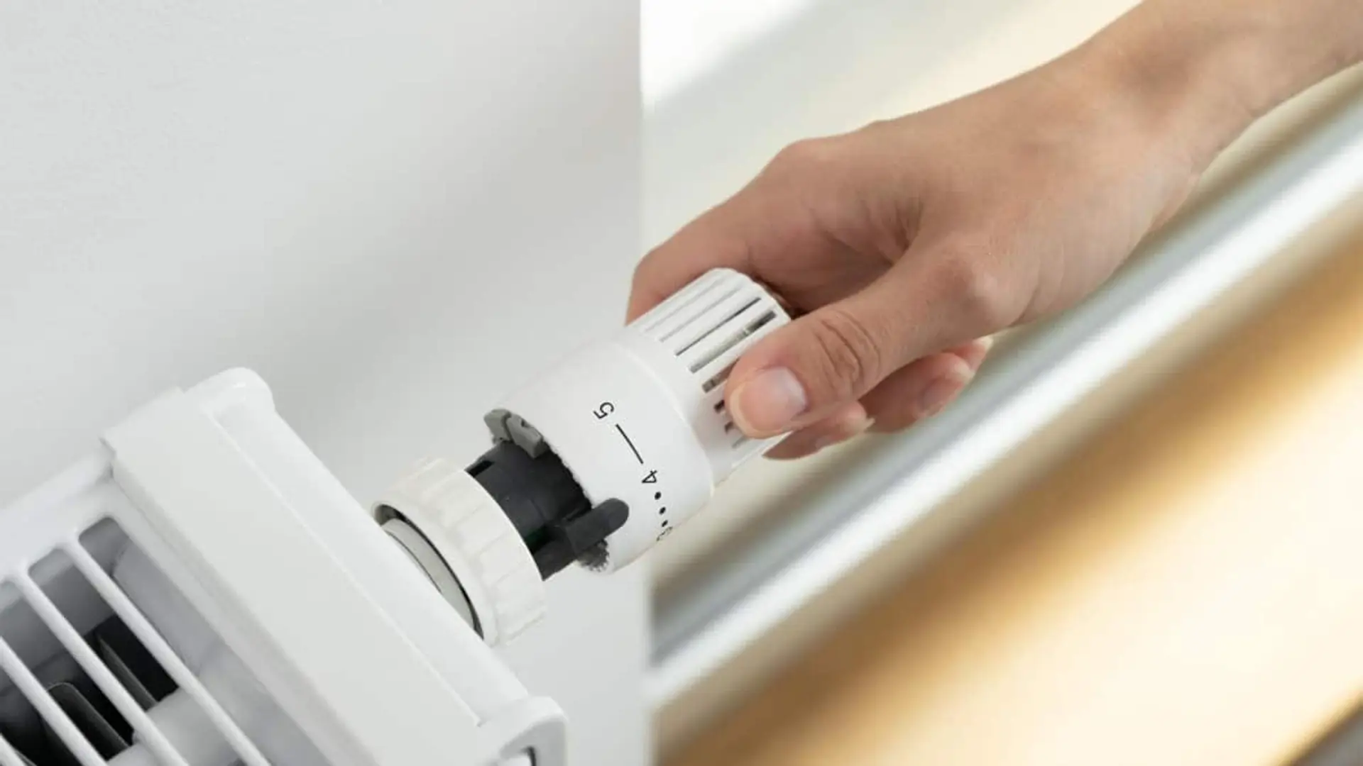 Mano ajustando el termostato de un radiador para regular la temperatura de la calefacción en casa.
