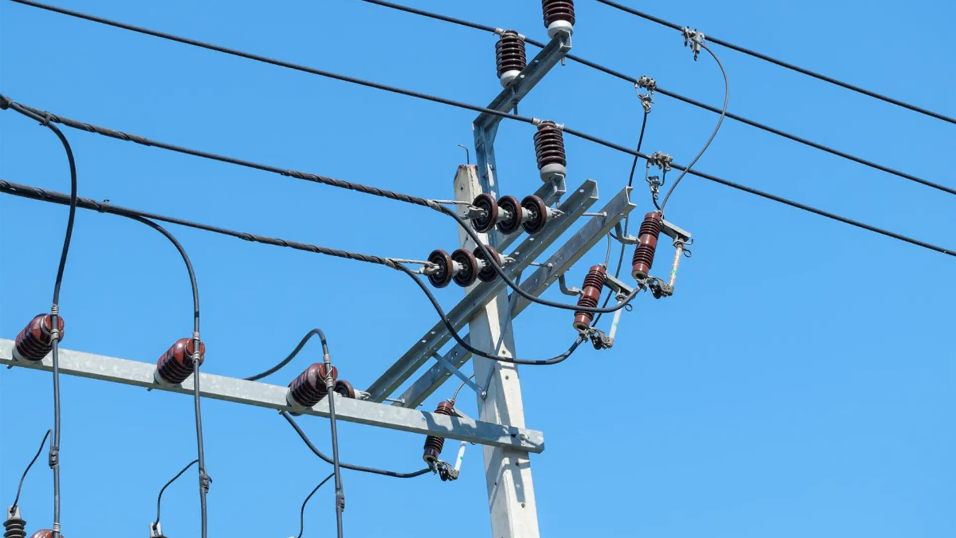 Detalle de una línea eléctrica de media tensión con aisladores y cableado sobre un poste bajo cielo despejado.