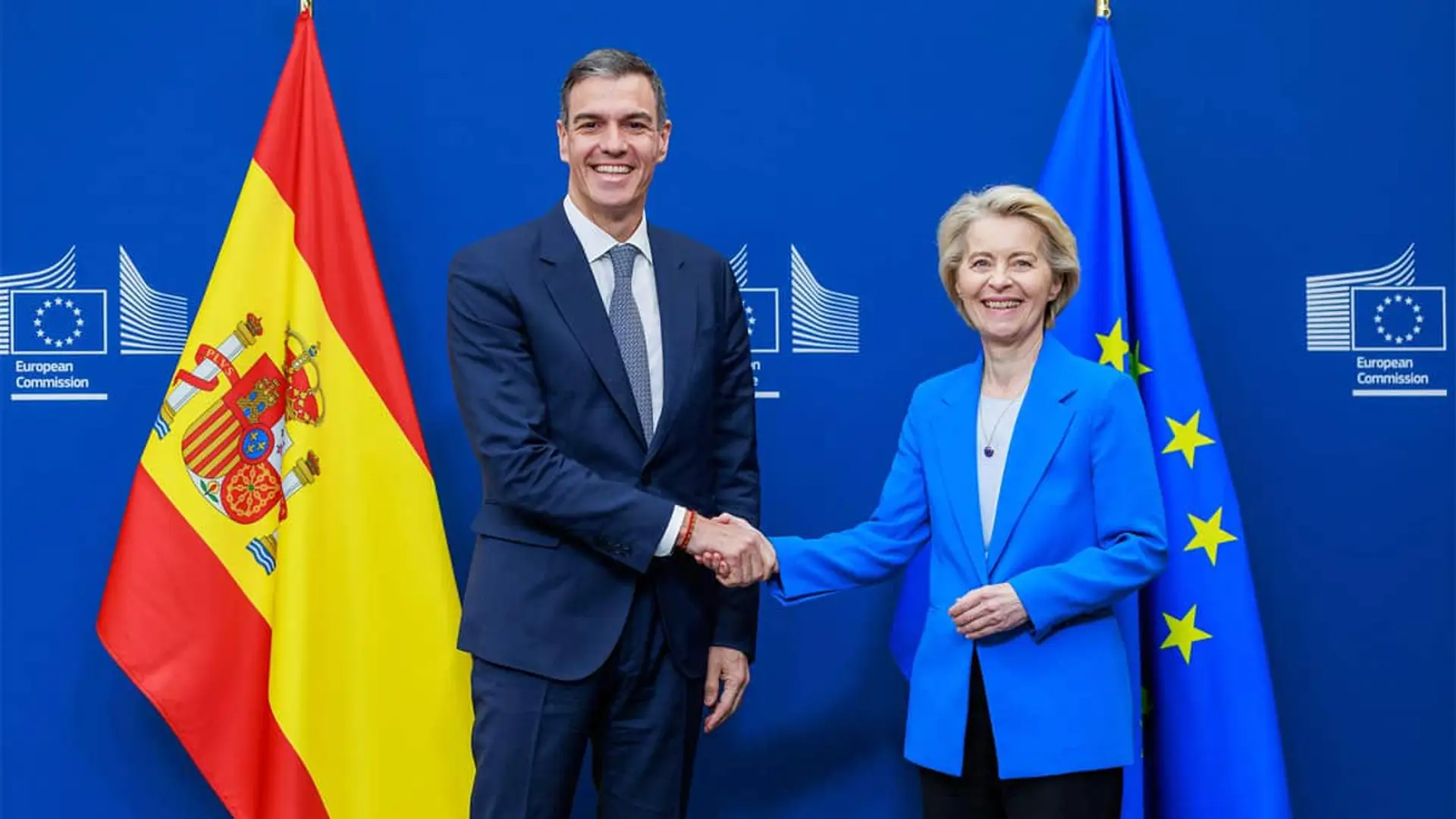 Pedro Sánchez y Ursula Von der Leyen se dan la mano delante de las banderas de España y la Unión Europea.