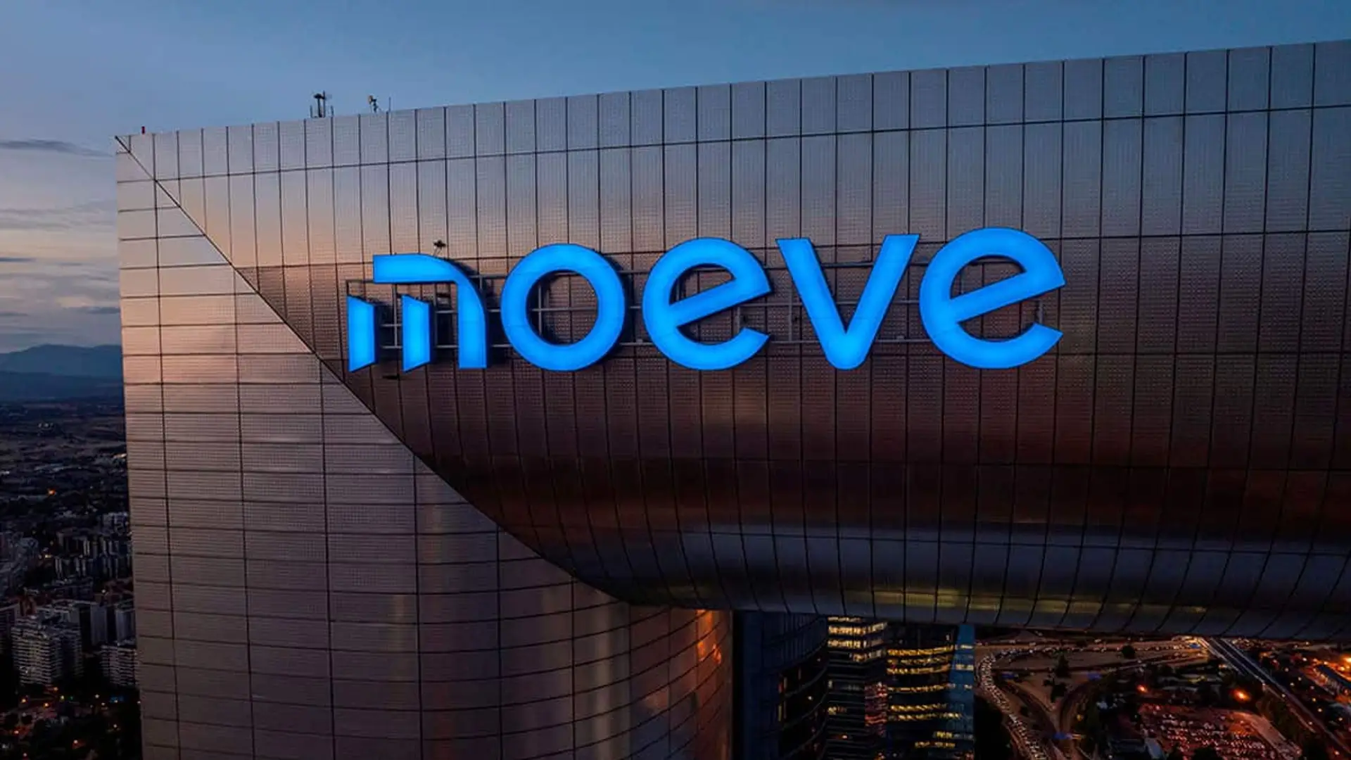Fachada de un edificio corporativo con el logotipo iluminado de Moeve al atardecer.