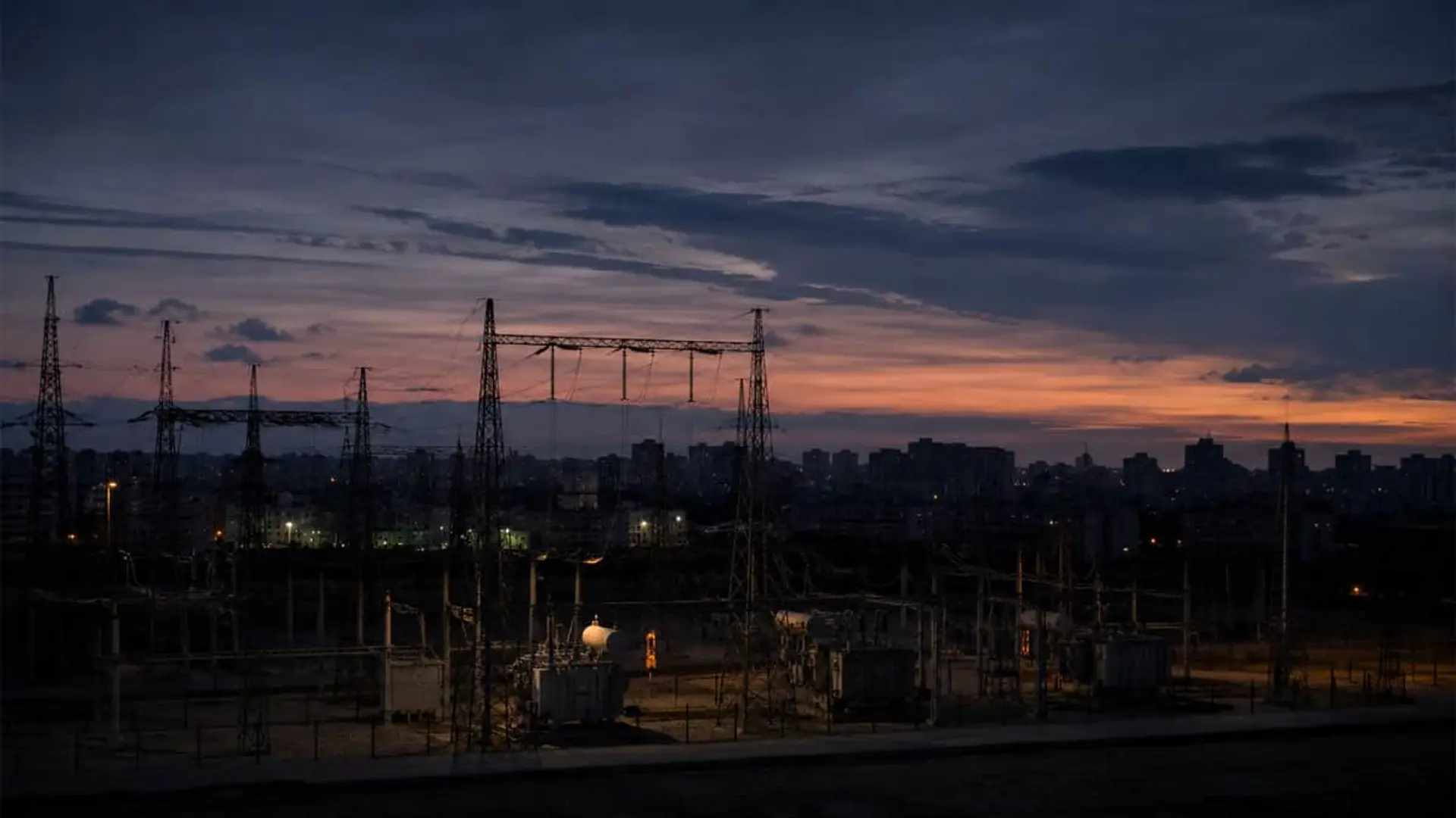 La CNMC descarta que pague el Estado: los 38,7 millones del apagón irán a la factura de la luz Subestación eléctrica urbana al atardecer con torres de alta tensión y skyline de la ciudad.