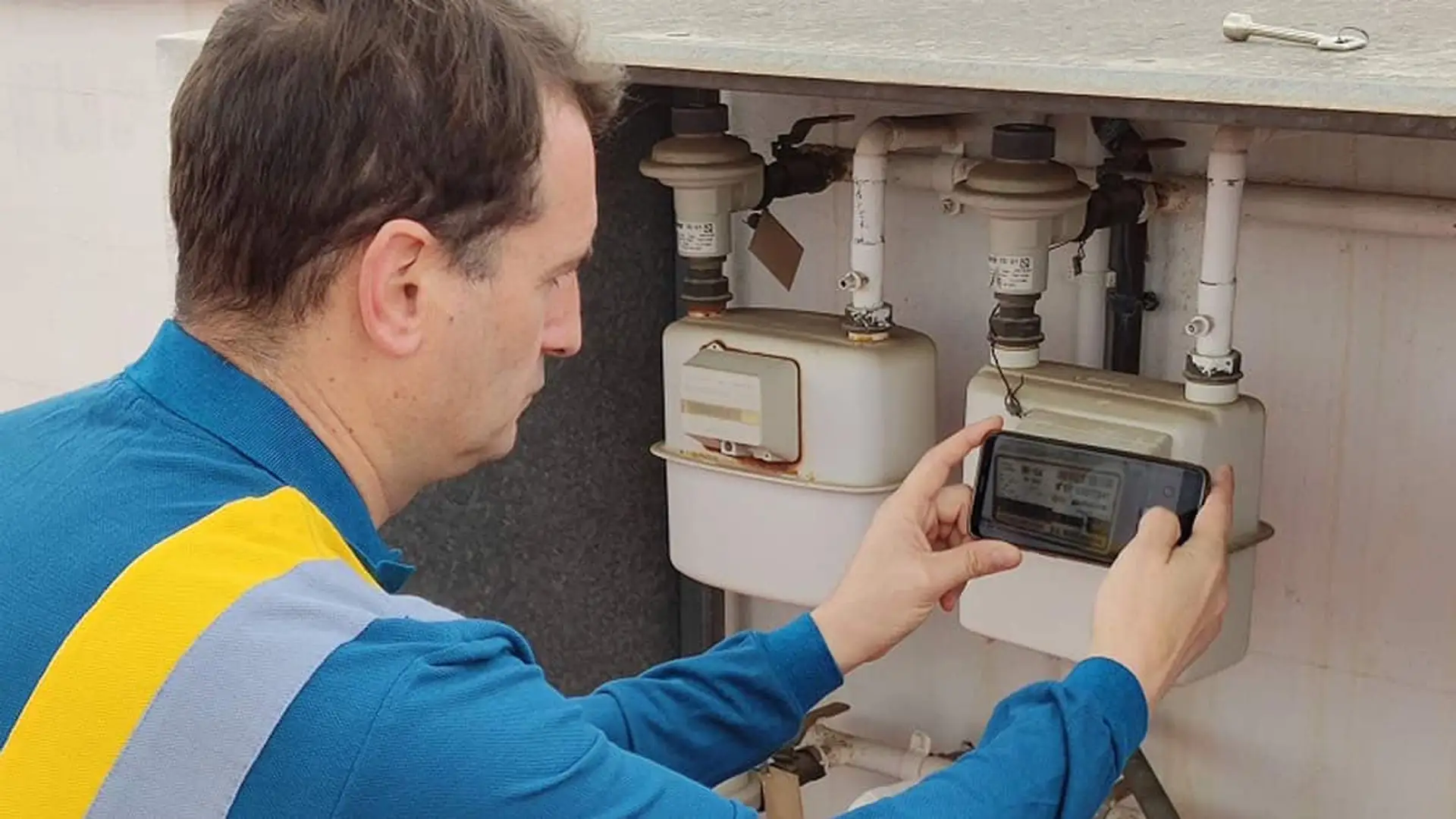 Trabajador tomando una lectura del contador de gas natural con su teléfono móvil durante una revisión técnica.