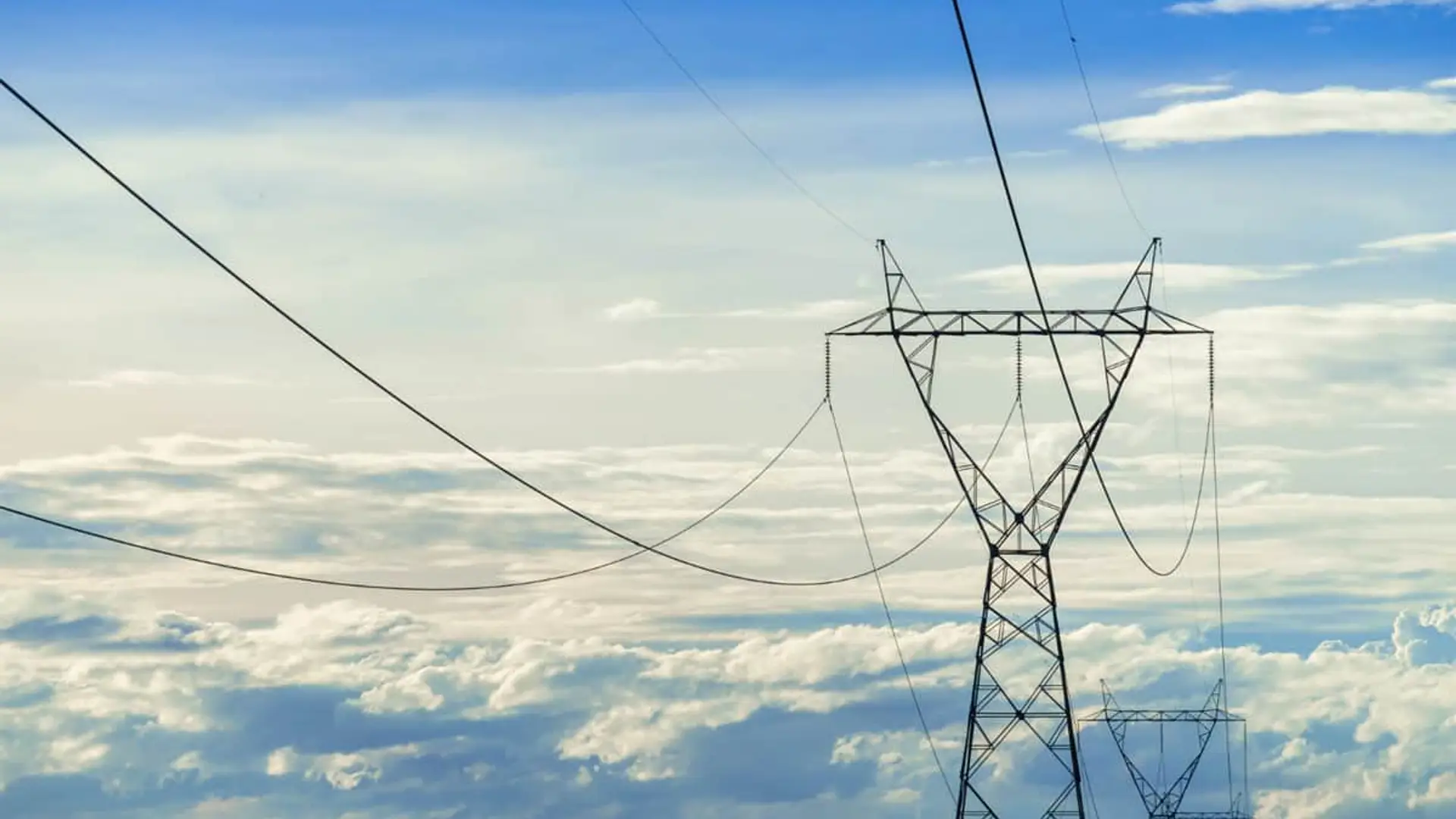 Alerta máxima de Red Eléctrica: España ante un nuevo riesgo de apagón por fallos de tensión Torres y cables de alta tensión eléctrica sobre un cielo parcialmente nublado.