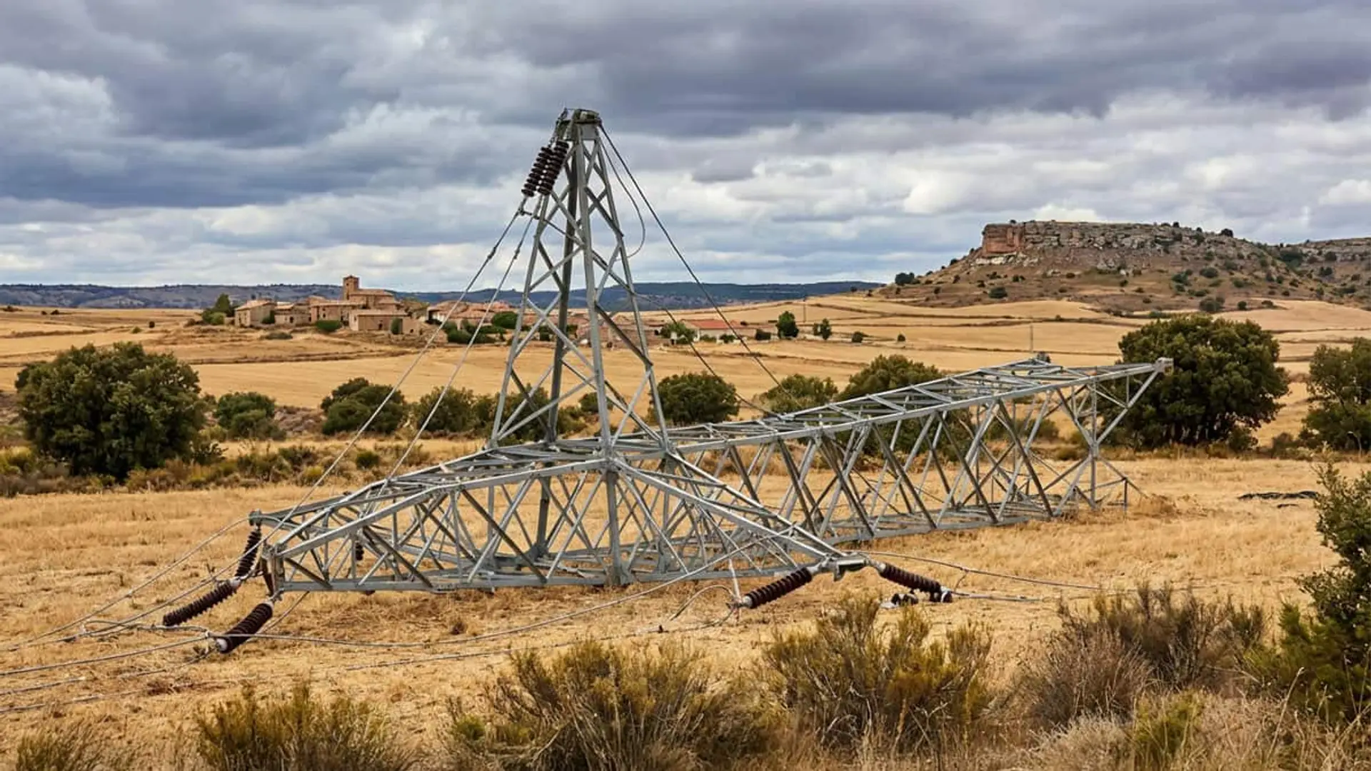 Así es el plan de emergencia que la CNMC acaba de aprobar para evitar otro gran apagón en España Torre eléctrica de alta tensión caída en una zona rural de campo seco, con cables derribados y paisaje agrícola al fondo.