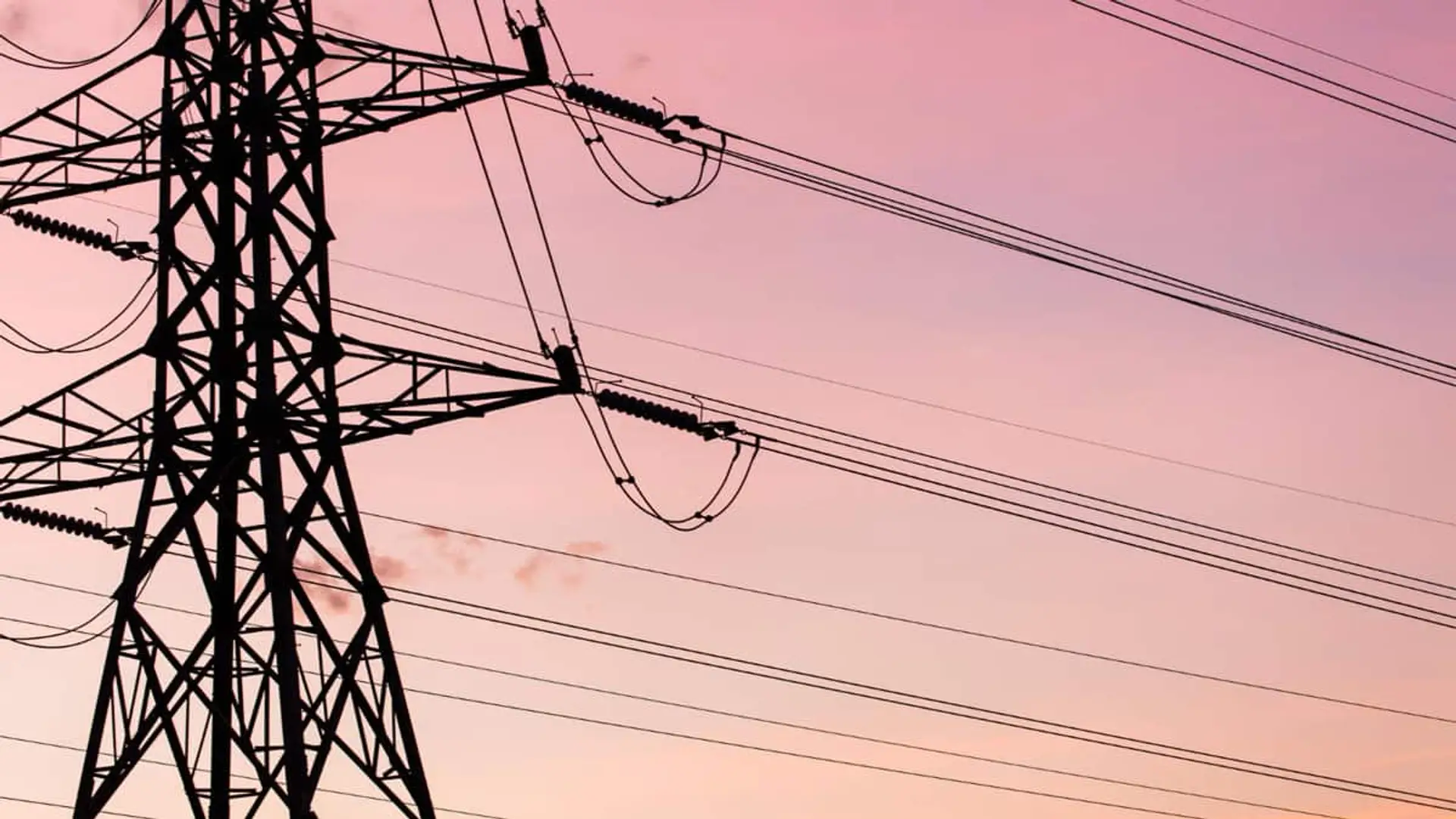 Torre eléctrica con líneas de transmisión sobre cielo rosado al atardecer