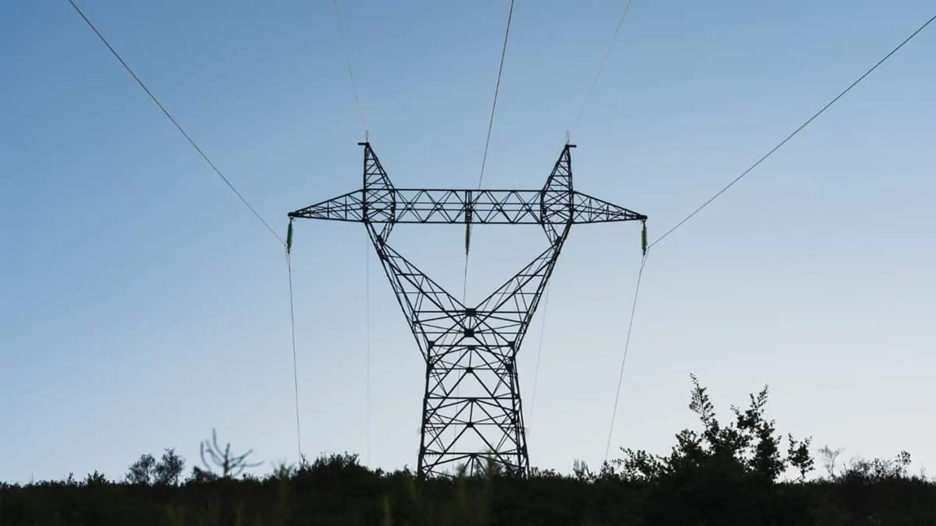 Torre eléctrica de alta tensión bajo un cielo azul y sobre un entorno de vegetación verde.