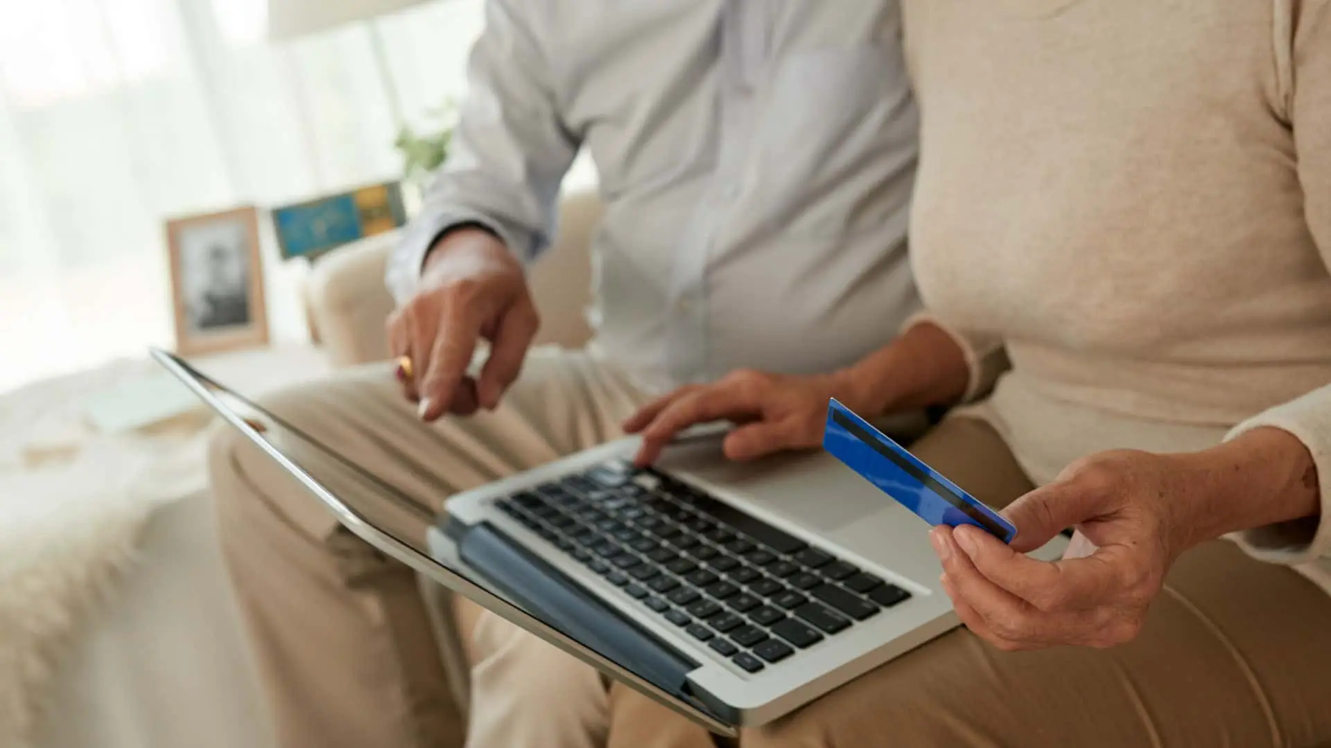 Pareja senior gestionando sus finanzas o pagando una factura online con un portátil y una tarjeta. Banca digital para la tercera edad.