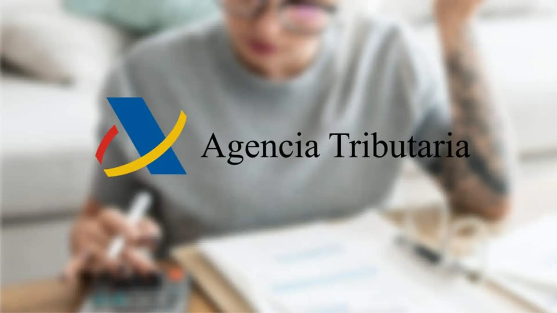 Logotipo de la Agencia Tributaria sobre la imagen de una persona calculando impuestos en casa.