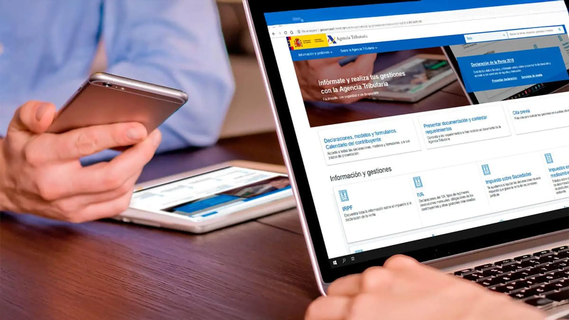 Persona usando portátil y smartphone para navegar por la web oficial de la Agencia Tributaria y realizar trámites del IRPF.